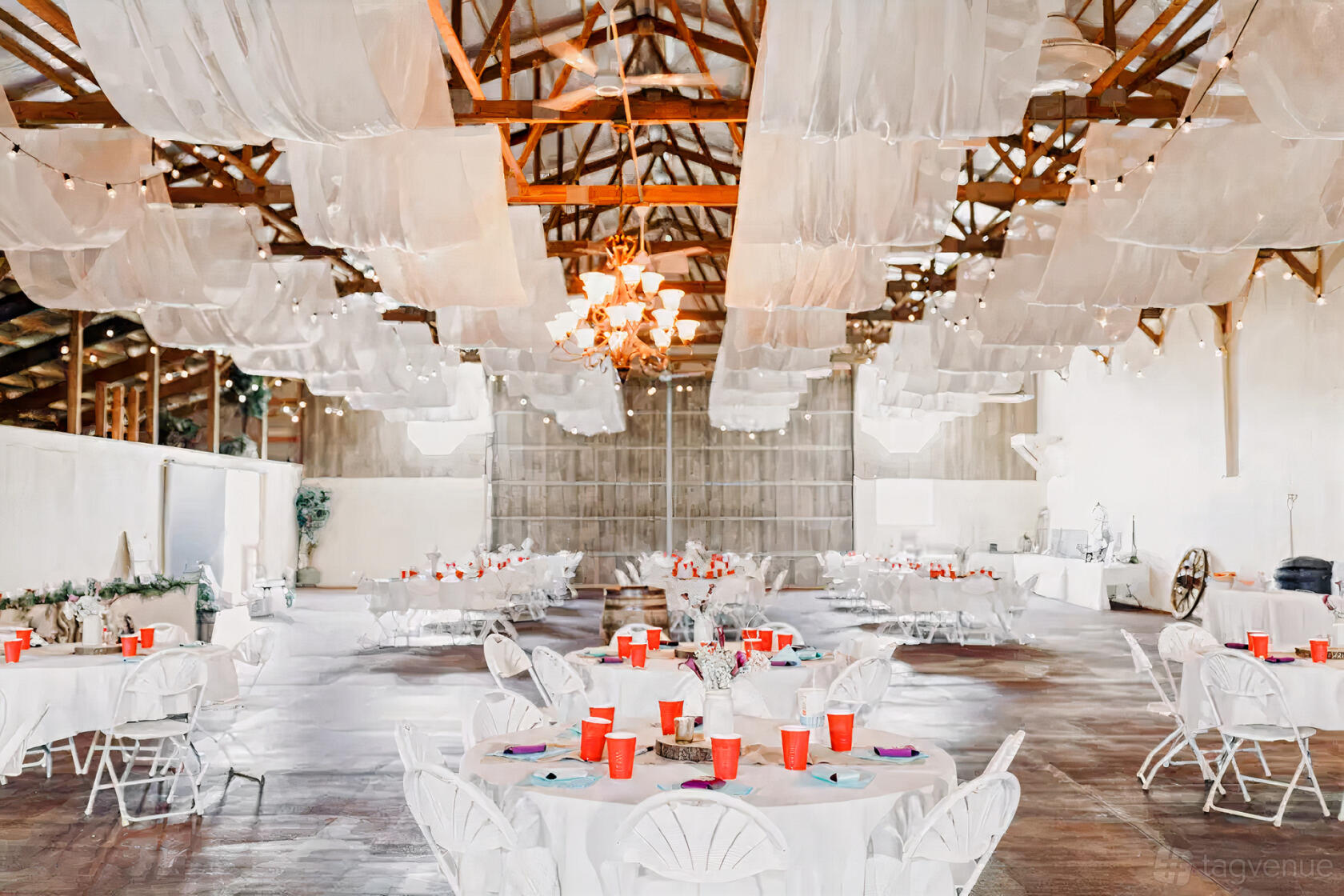An event venue with draped white fabric ceiling, exposed wooden beams, round tables, and red cups at BrighterDaze.