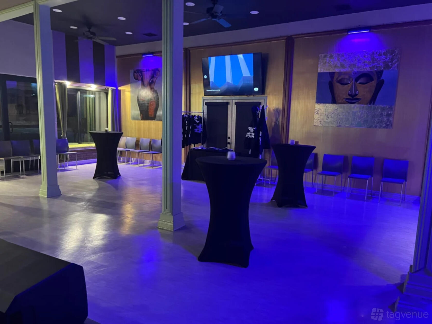 An event venue with cocktail tables, rows of chairs, blue accent lighting, and modern art at The Nile Spot.