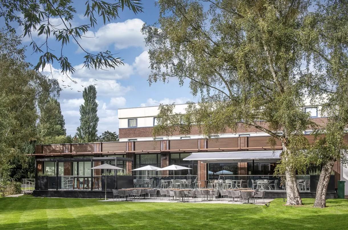 An outdoor terrace with tables, chairs, and umbrellas overlooking a lawn at Holiday Inn Shepperton.