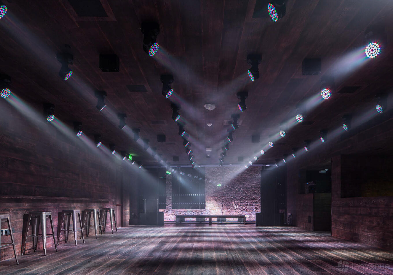 A basement event space with wood-paneled walls, spotlight ceiling lighting, and high stools at London EDITION.