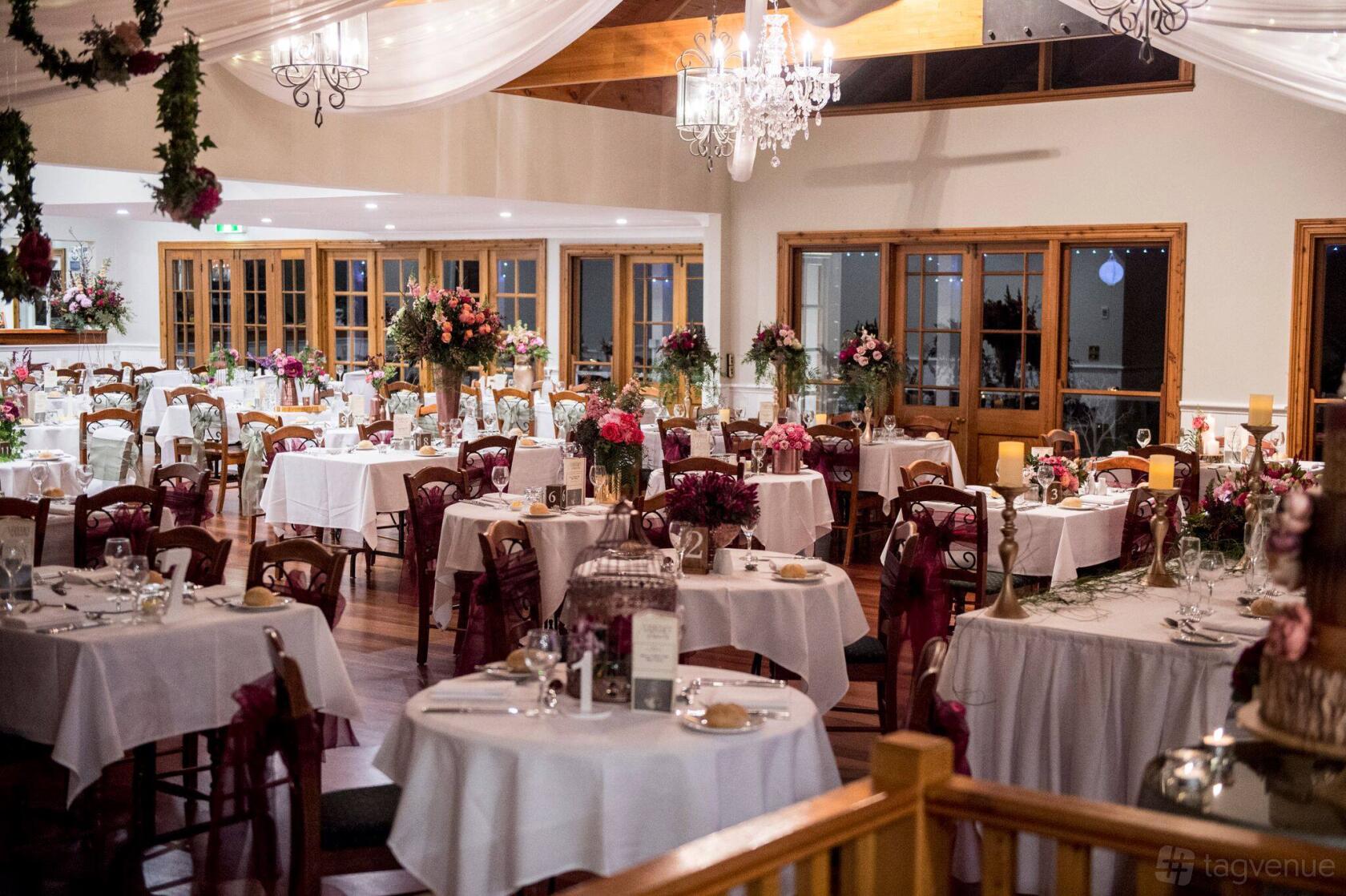 An event venue with chandeliers, draped ceilings, floral centerpieces, and wooden chairs at Loxley on Bellbird Hill.
