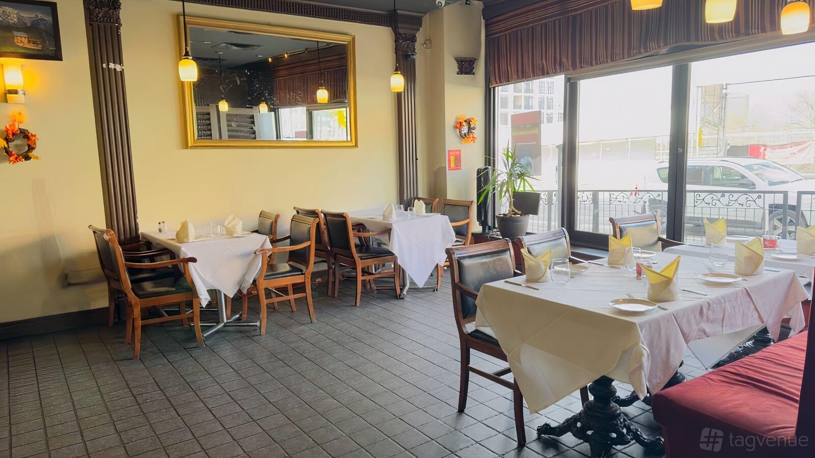 A restaurant dining area with white tablecloths, wooden chairs, and large windows at Durbar Indian Cuisine.