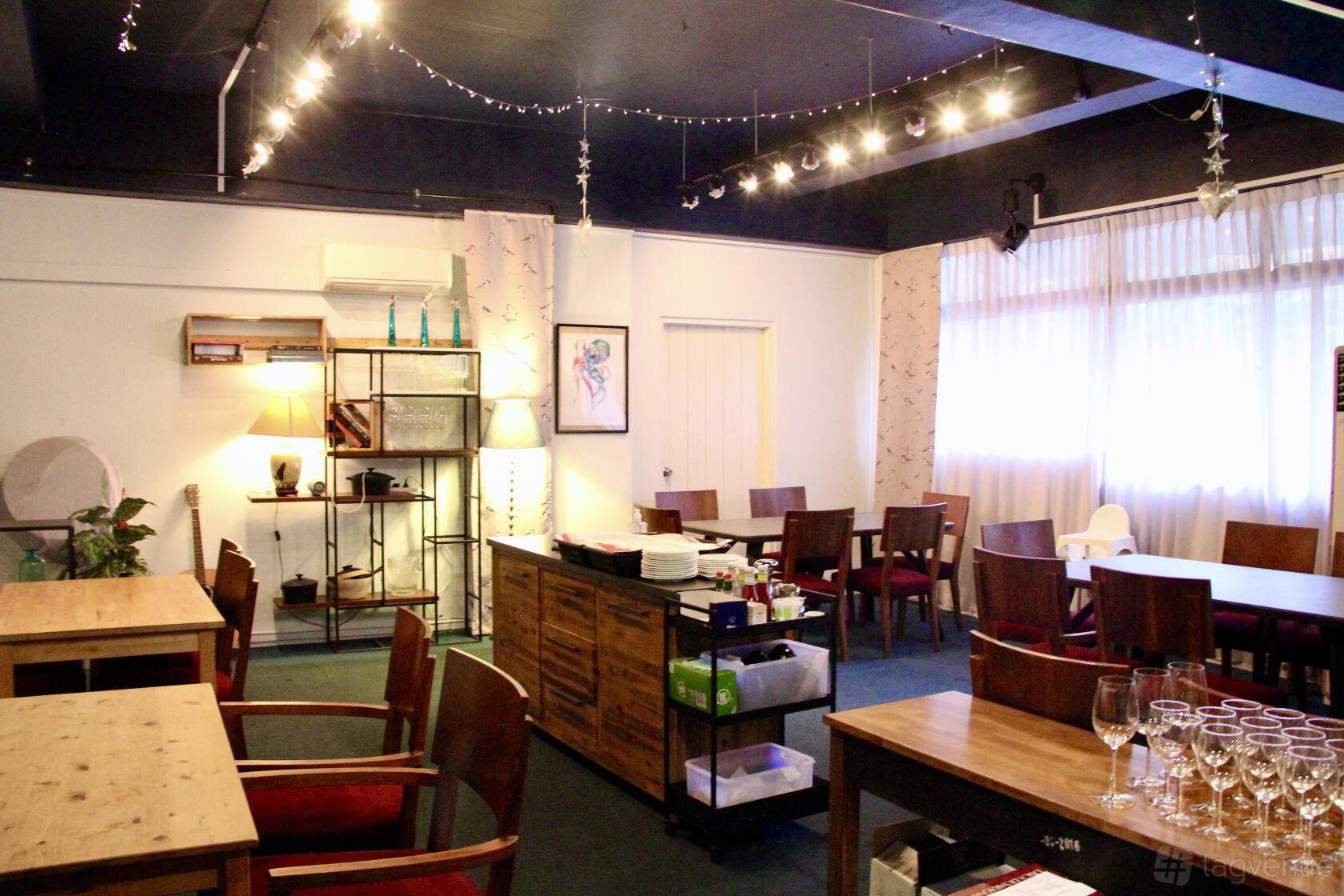 A function room with wooden tables, string lights, and floor-to-ceiling windows at Micasa Kitchen and Bar.