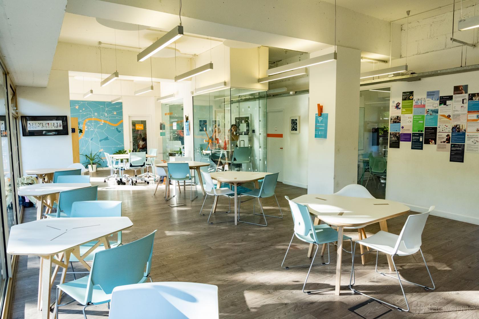 A coworking space with light wood floors, blue chairs, and wall-mounted bulletin boards at Health Foundry.