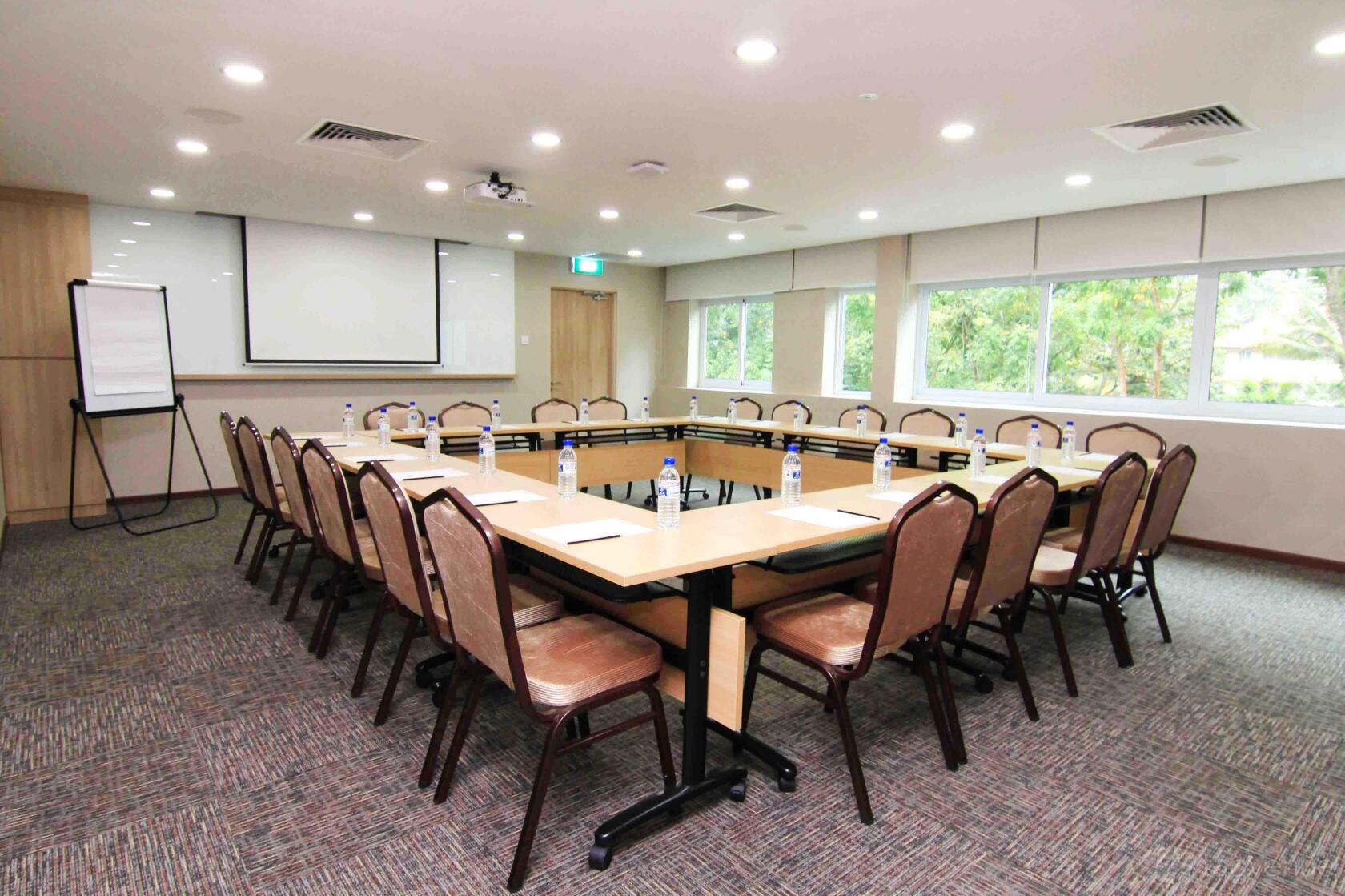 A meeting room with U-shaped tables, cushioned chairs, large windows, and a projector at Metropolitan YMCA Singapore.