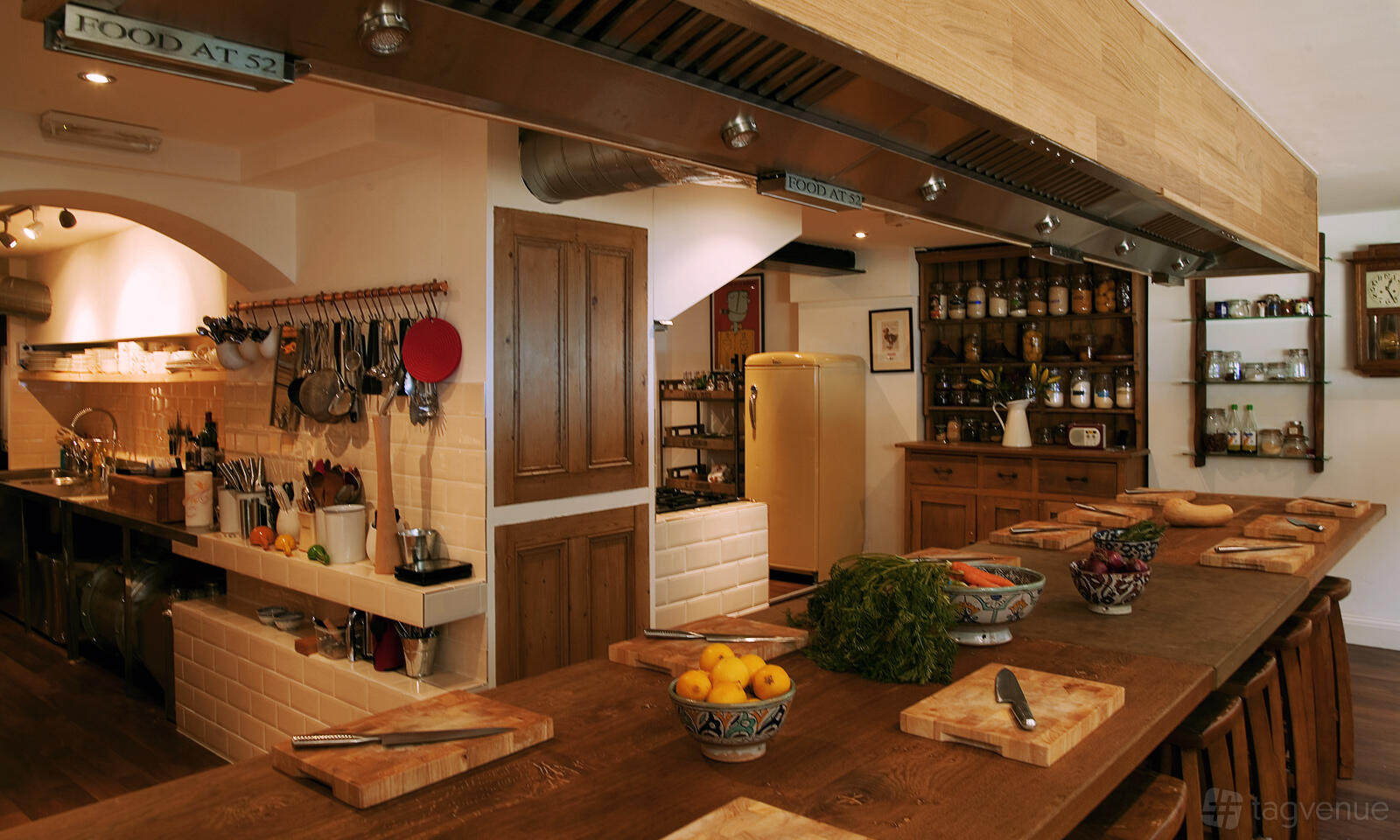 A spacious kitchen with wooden countertops, open shelving, hanging utensils, and bowls of fresh produce at Food at 52.
