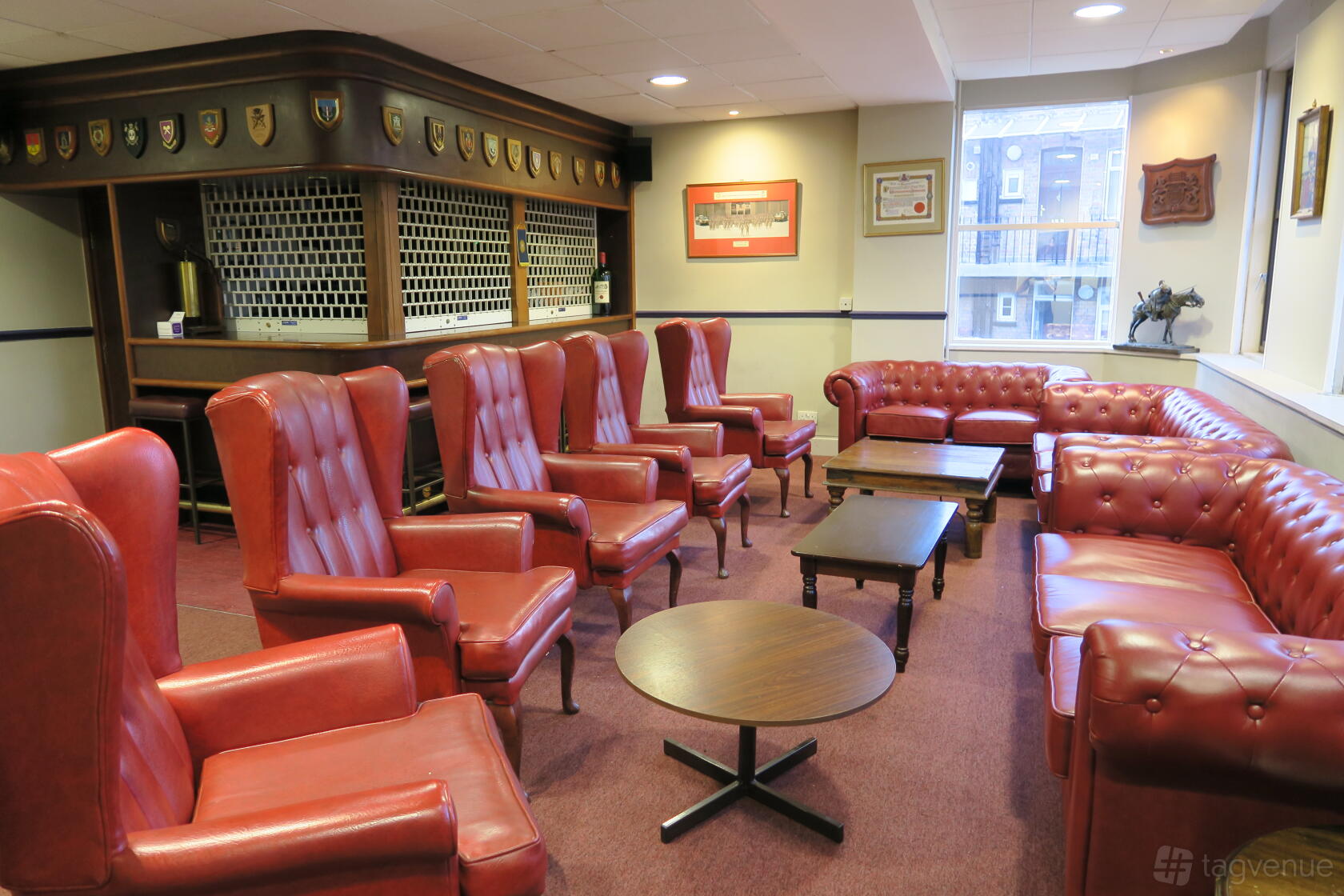 A meeting centre lounge with red leather armchairs, sofas, round tables, and wall plaques at Fulham, Fulham High Street.
