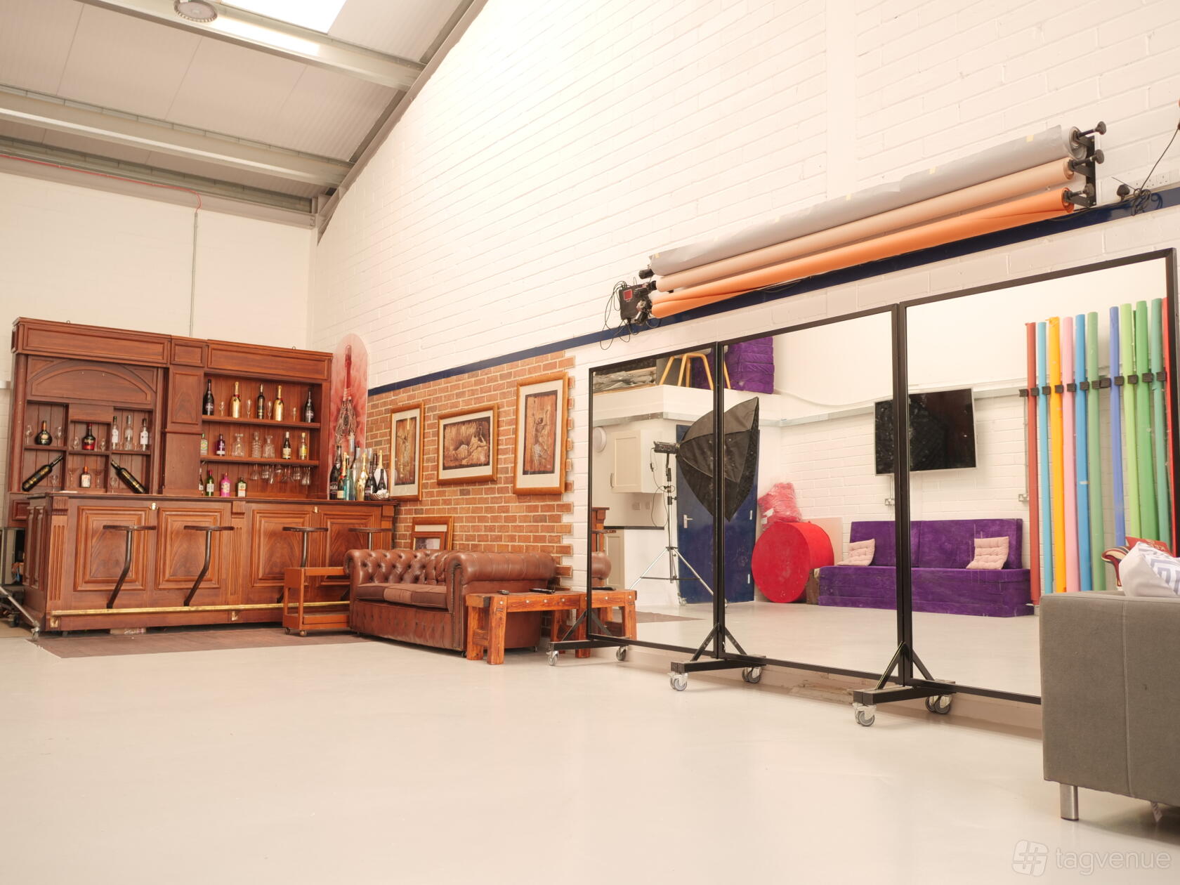 A photo studio with a wooden bar, brown leather sofa, wall art, and colorful backdrop rolls at Nameless Vision Studios.