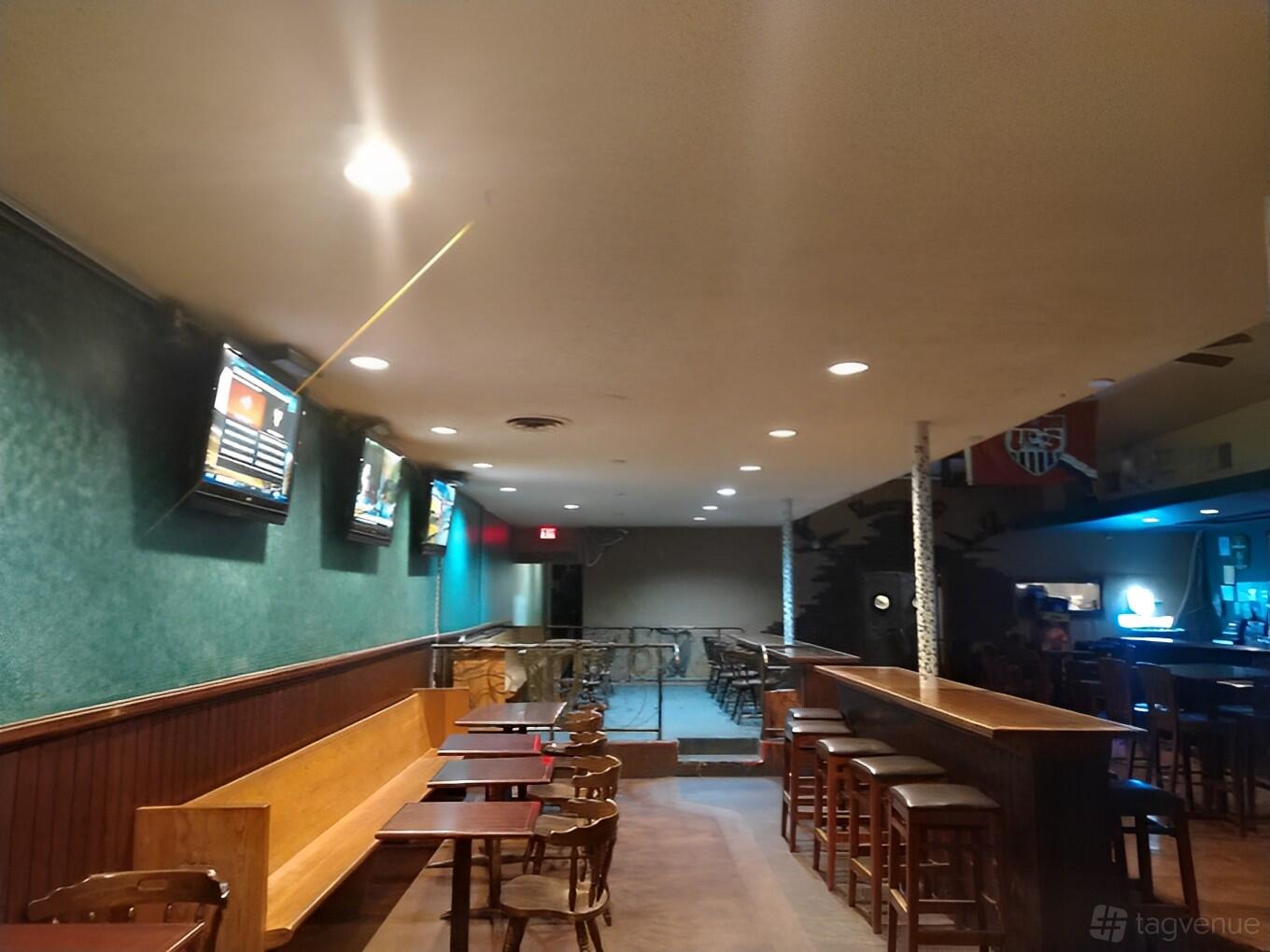A pub with green textured walls, wooden benches, high tables with stools, and TV screens at The Harp.