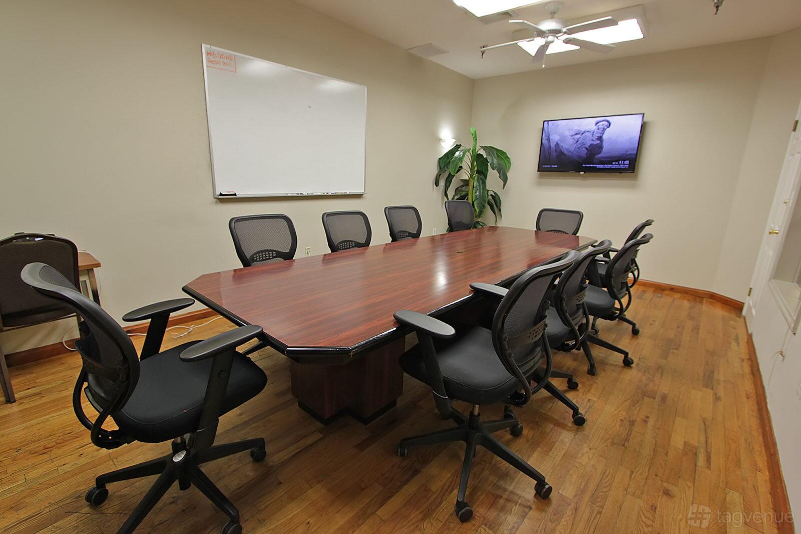 A coworking space conference room with a long wooden table, black mesh chairs, a whiteboard, and a wall-mounted TV at Coalition Space - Flatiron.