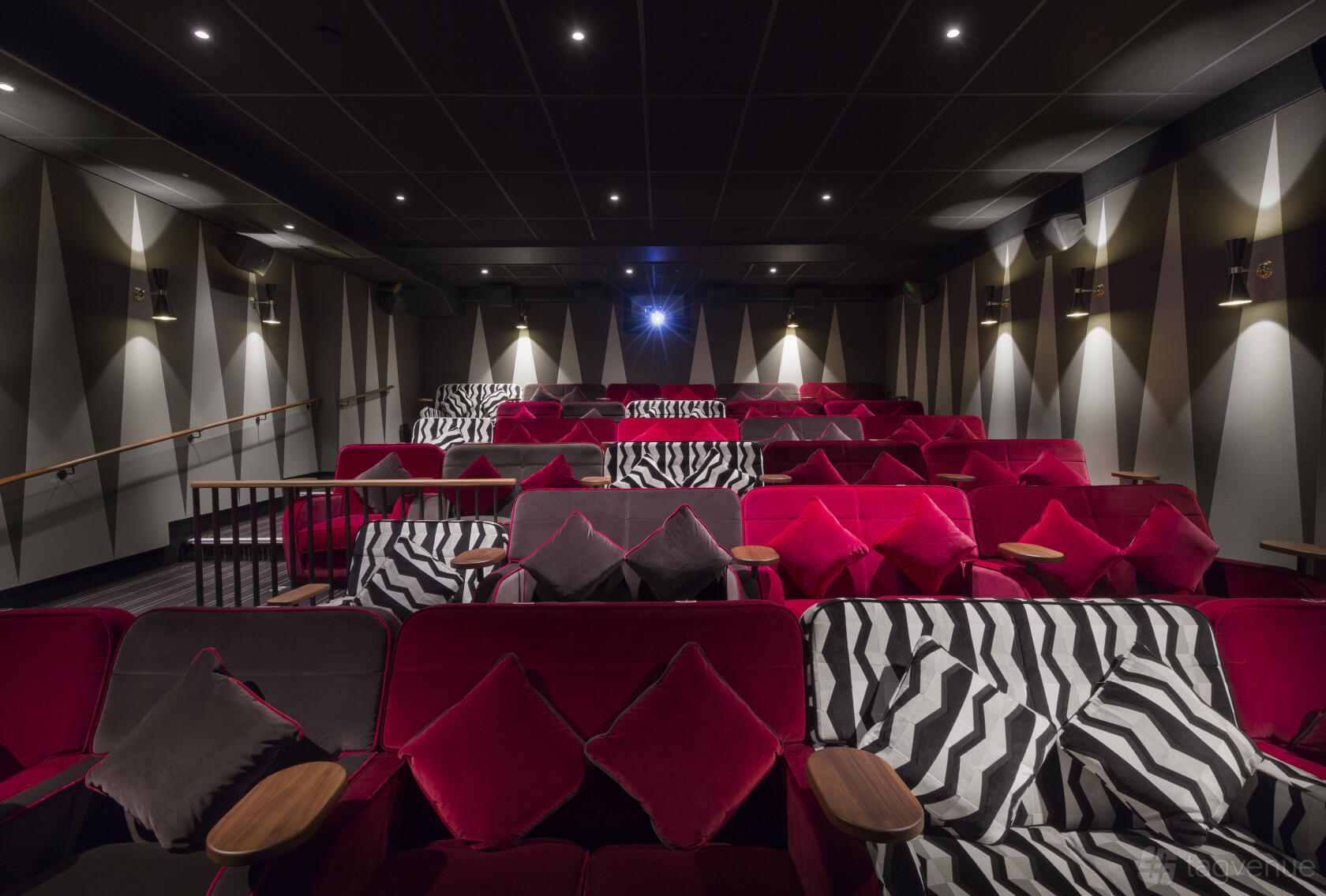 An auditorium with tiered red velvet seats, striped cushions, and individual wooden arm tables at Everyman Newcastle.