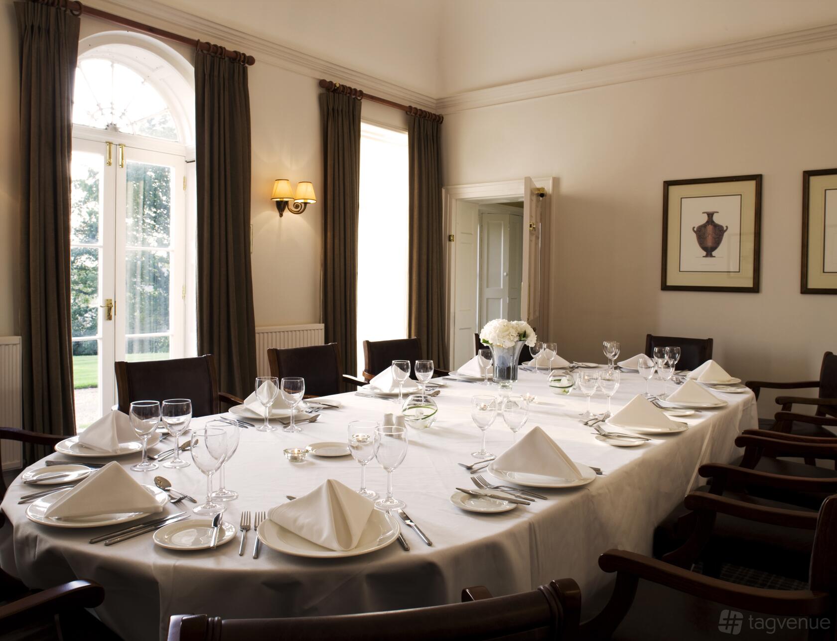 A meeting room with a large rectangular table set with white linens, glassware, and natural light at Highfield Park.