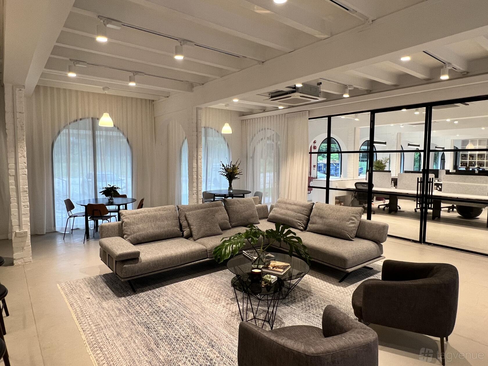 A lounge with gray sofas, a round coffee table, large arched windows, and white exposed beams at Thirdspace.