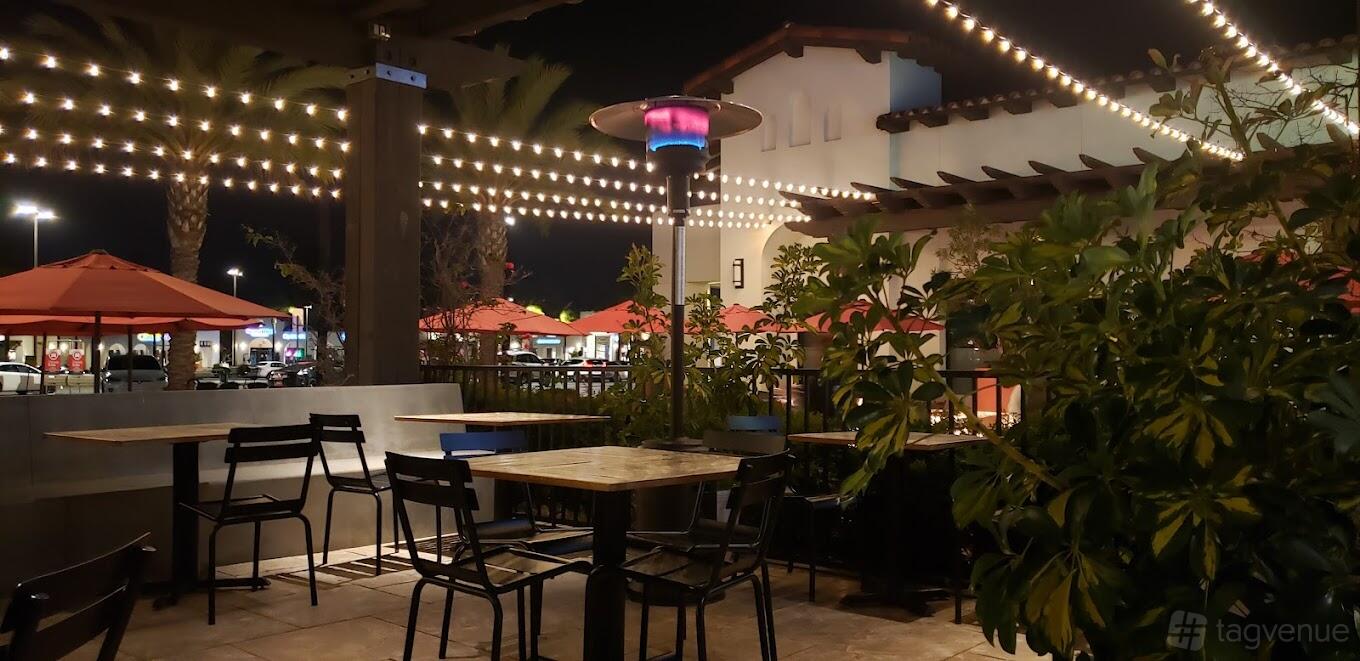 An outdoor restaurant patio with string lights, potted plants, and patio heaters at The Shop: Pizza and Cocktails.