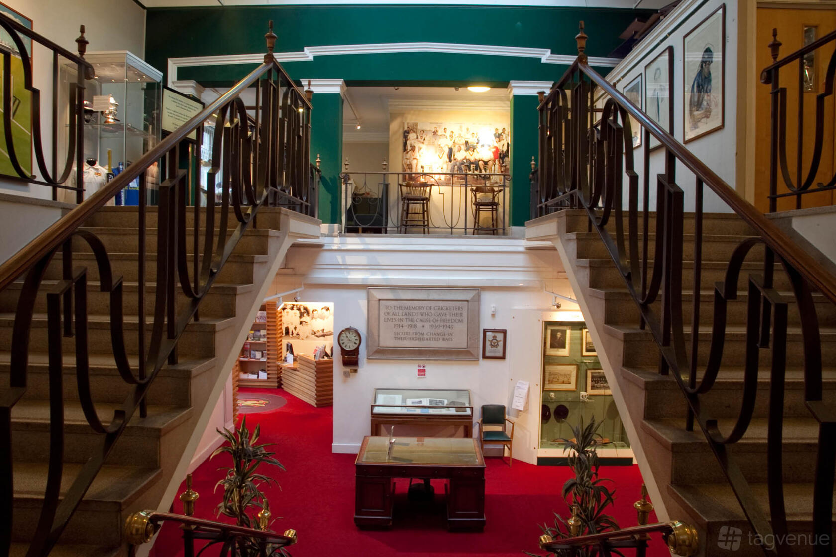 A historic event venue with a red carpeted staircase, framed memorabilia, and display cases at Lord's Cricket Ground.