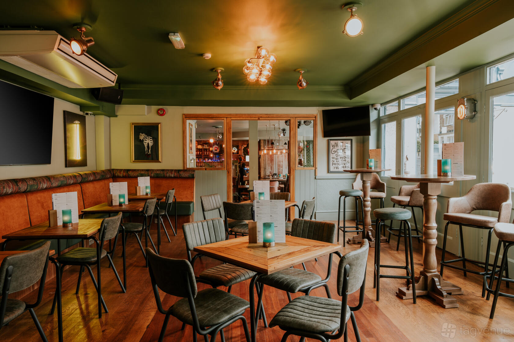 A pub with wooden floors, mixed-height tables, green walls, and natural light at Hawkins Forge.