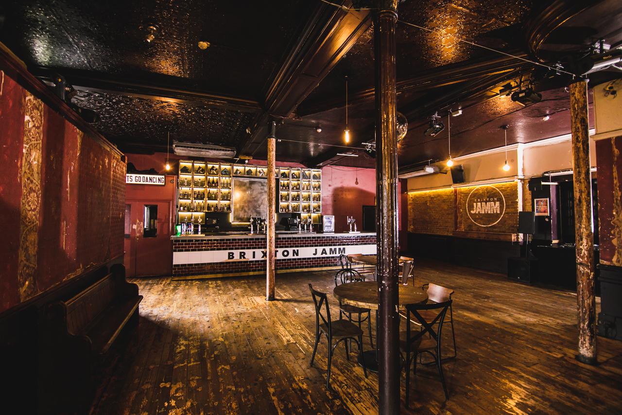 An event space in a nightclub with exposed brick walls, wooden floors, and a backlit bar at Brixton Jamm.