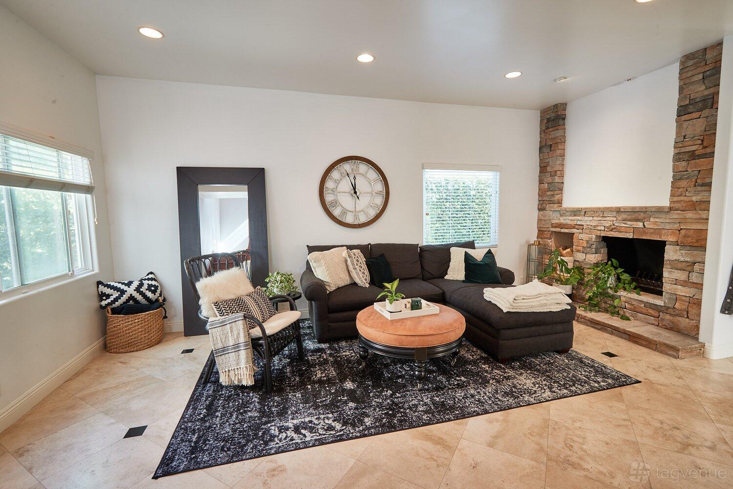 A photo studio with a sectional sofa, stone fireplace, large wall clock, and natural light at Beautiful 3-Story Home.