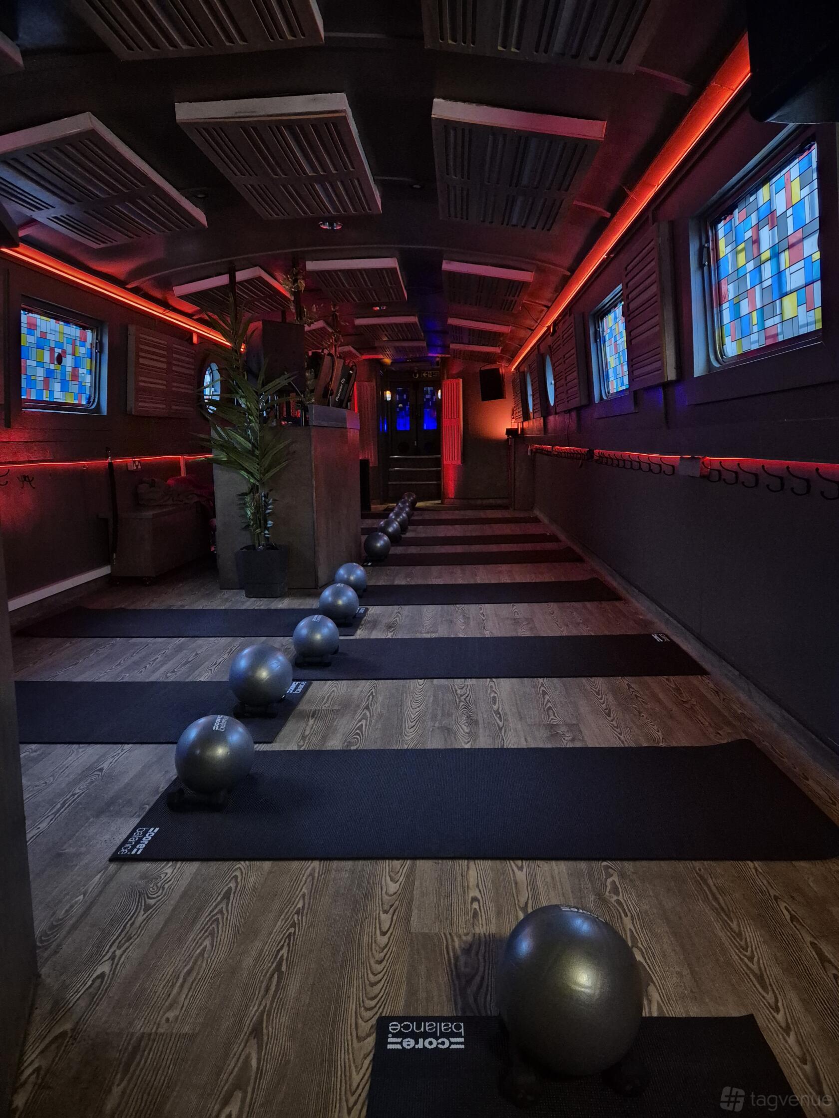 A boat with hardwood floors, yoga mats, exercise balls, and red accent lighting at The Goose.