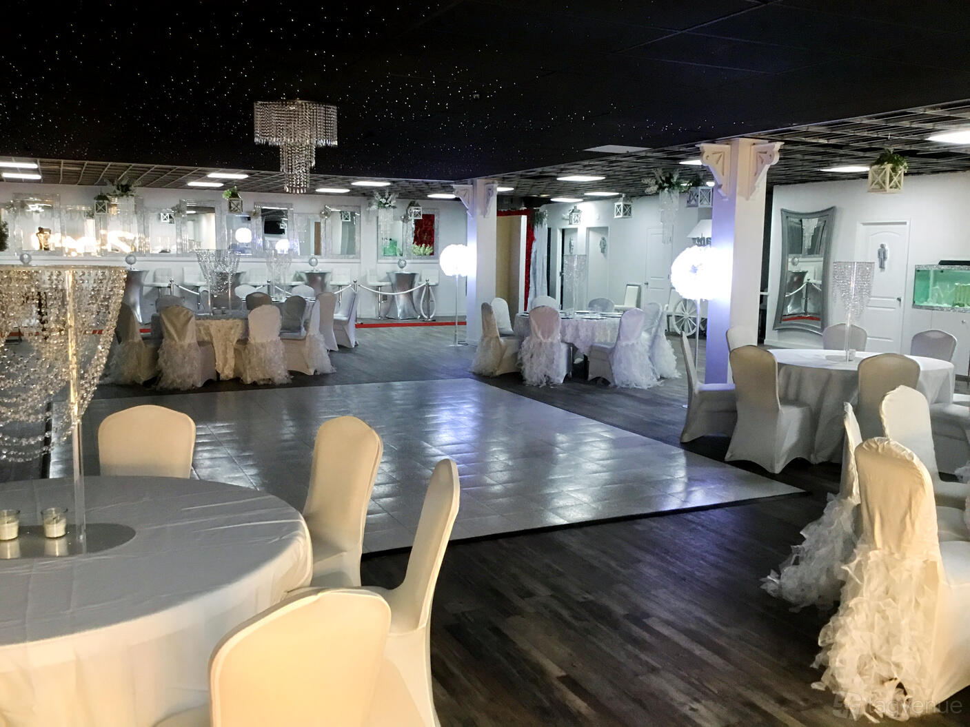 An event space in a hall with round tables draped in white linens and a dance floor at Mae's Liberty Palace.