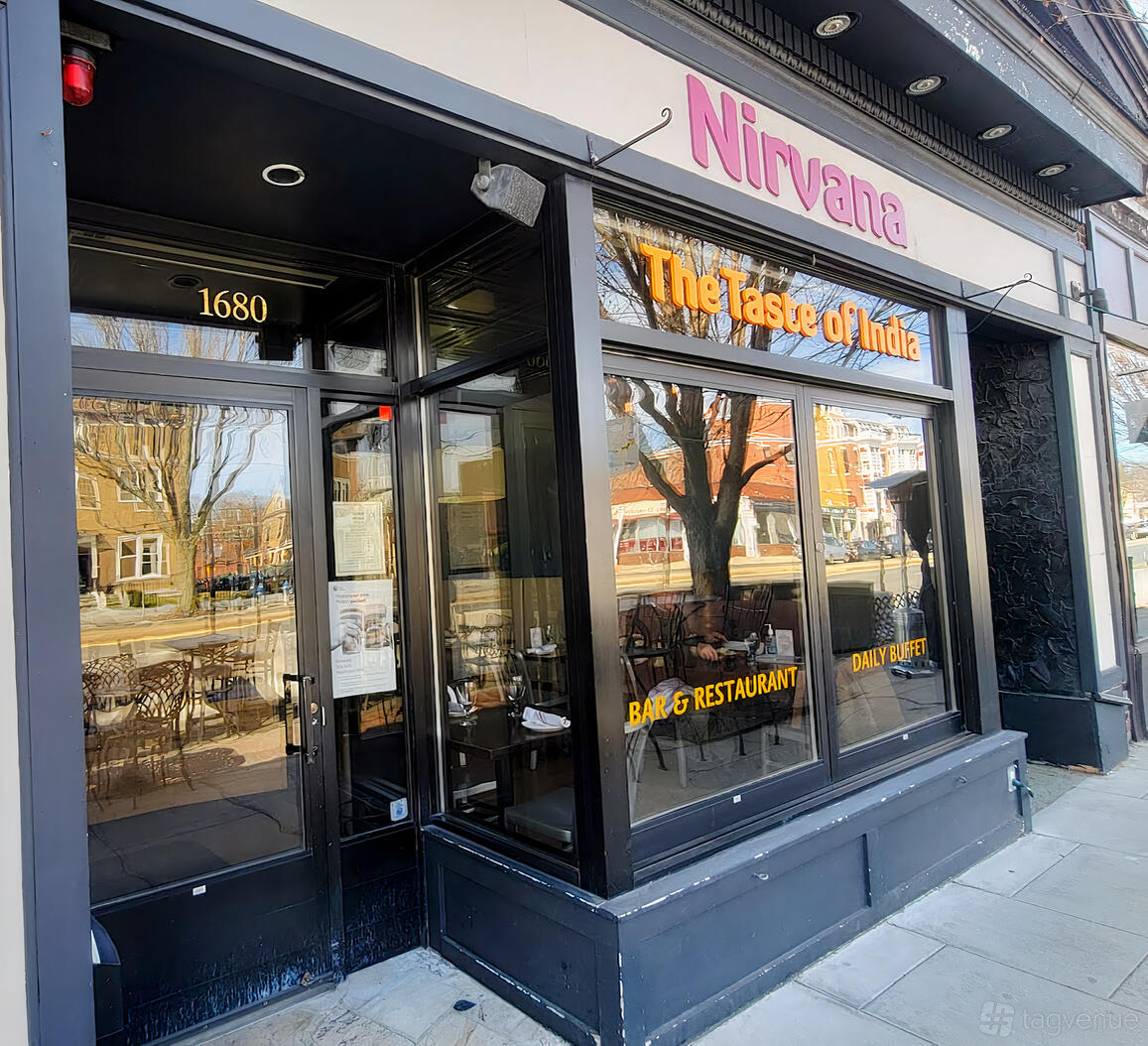 A restaurant exterior with large windows reflecting trees and the street at Nirvana: The Taste of India.