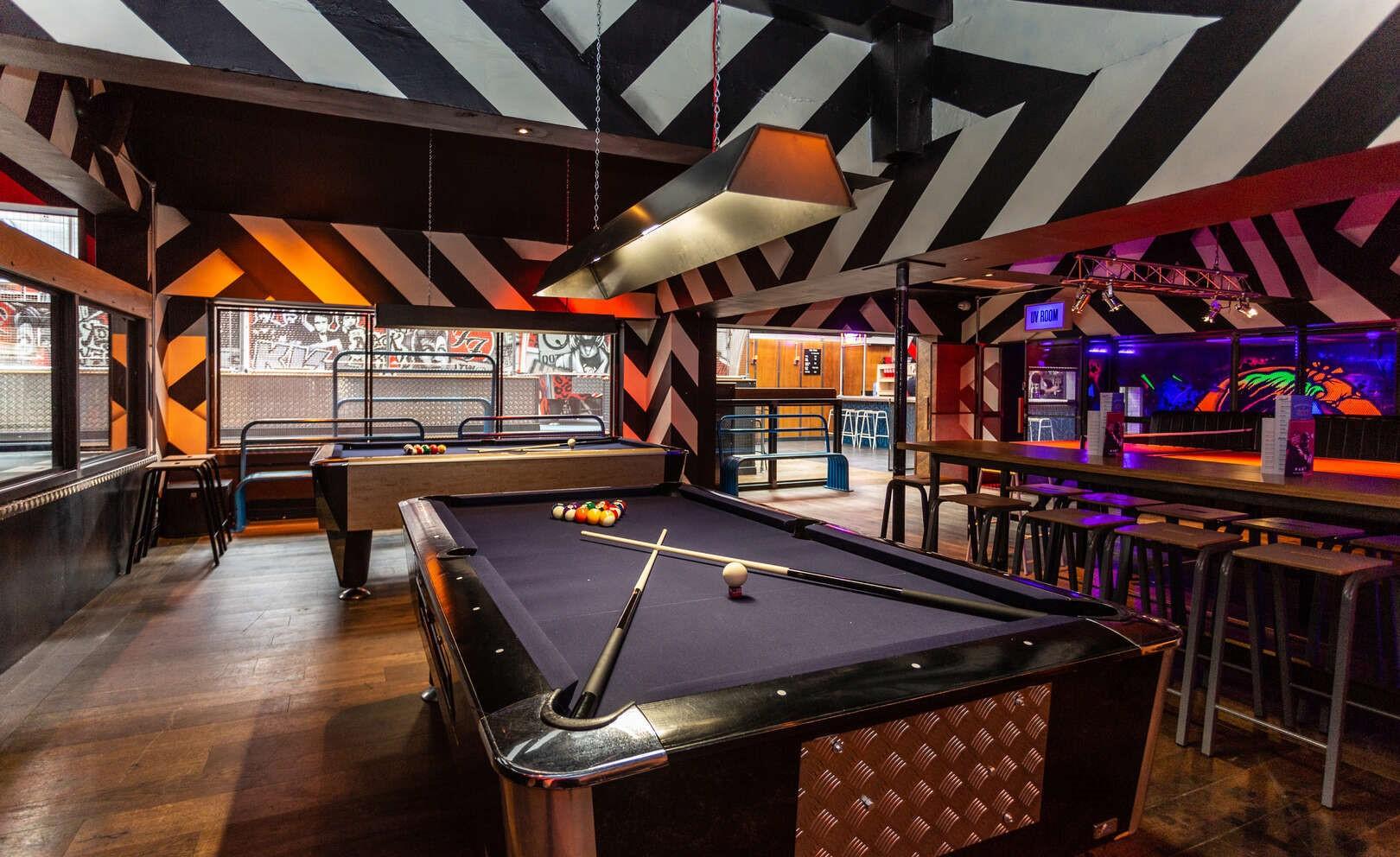 A bar with a black pool table, high stools, bold geometric wall patterns, and neon lighting at Roxy Ball Room Leeds Merrion Street.