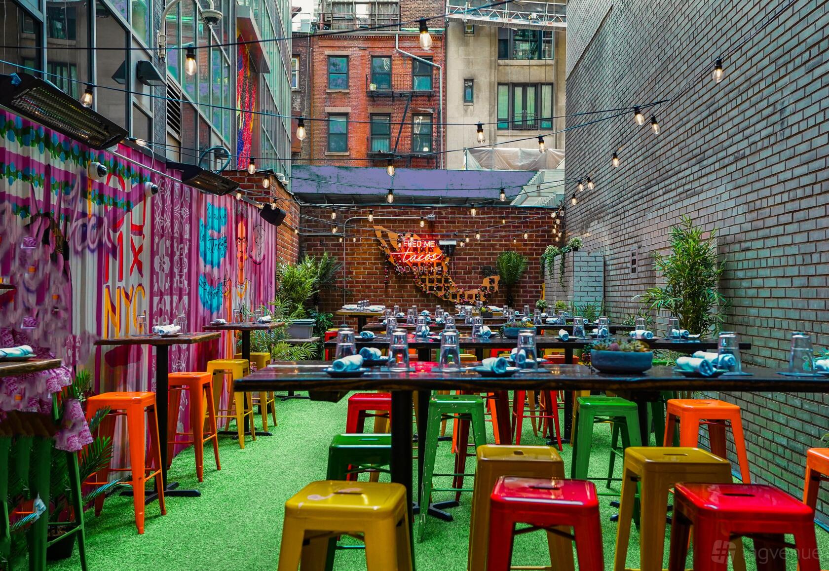 An outdoor restaurant with colorful metal stools, mural walls, and string lights at Toro Loco.