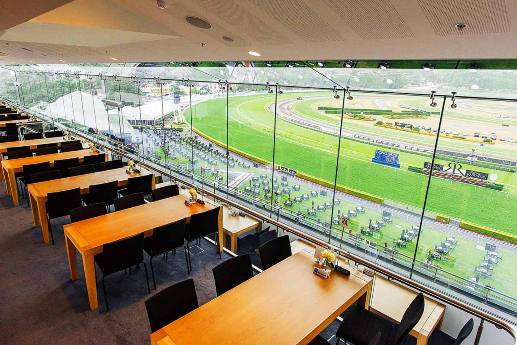 An event venue with floor-to-ceiling windows, wooden tables, and views overlooking the racecourse at Australian Turf Club @ Royal Randwick.