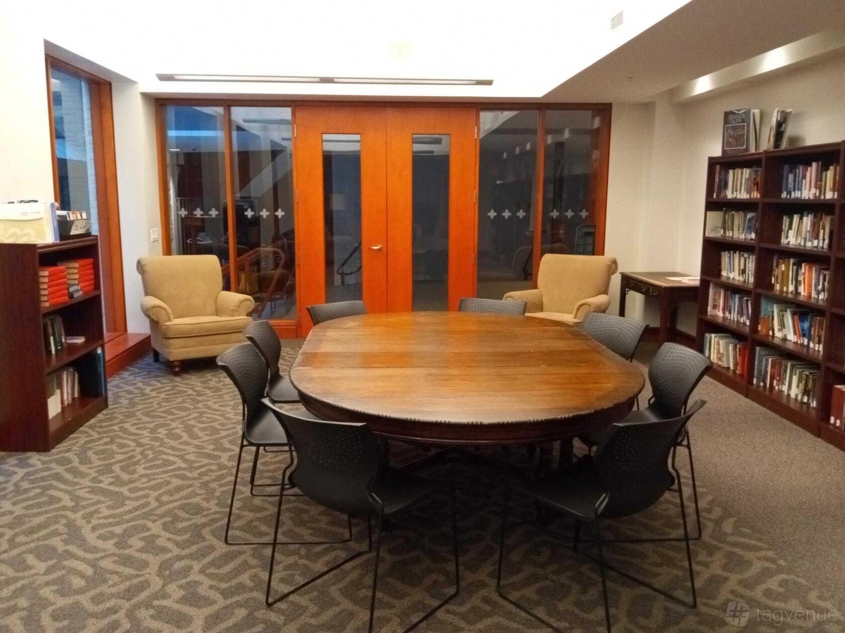 A meeting room with a round wooden table, eight chairs, bookshelves, and two upholstered armchairs at St. Paul's Bloor Street.