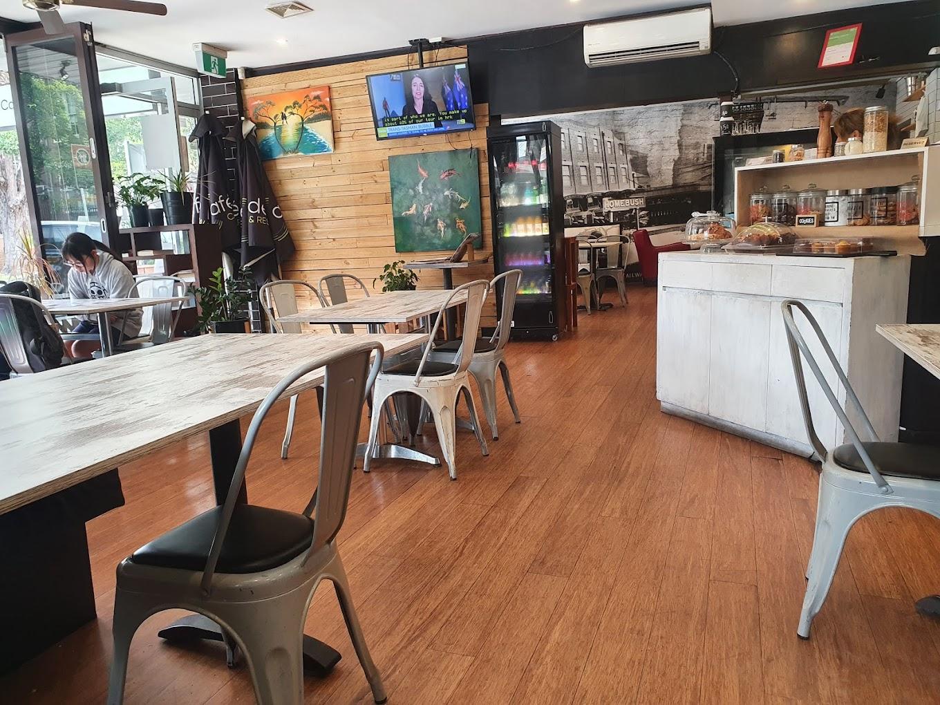 A cafe with wooden floors, metal chairs, artwork on the walls, and a counter displaying pastries at Cafe Tabouli.