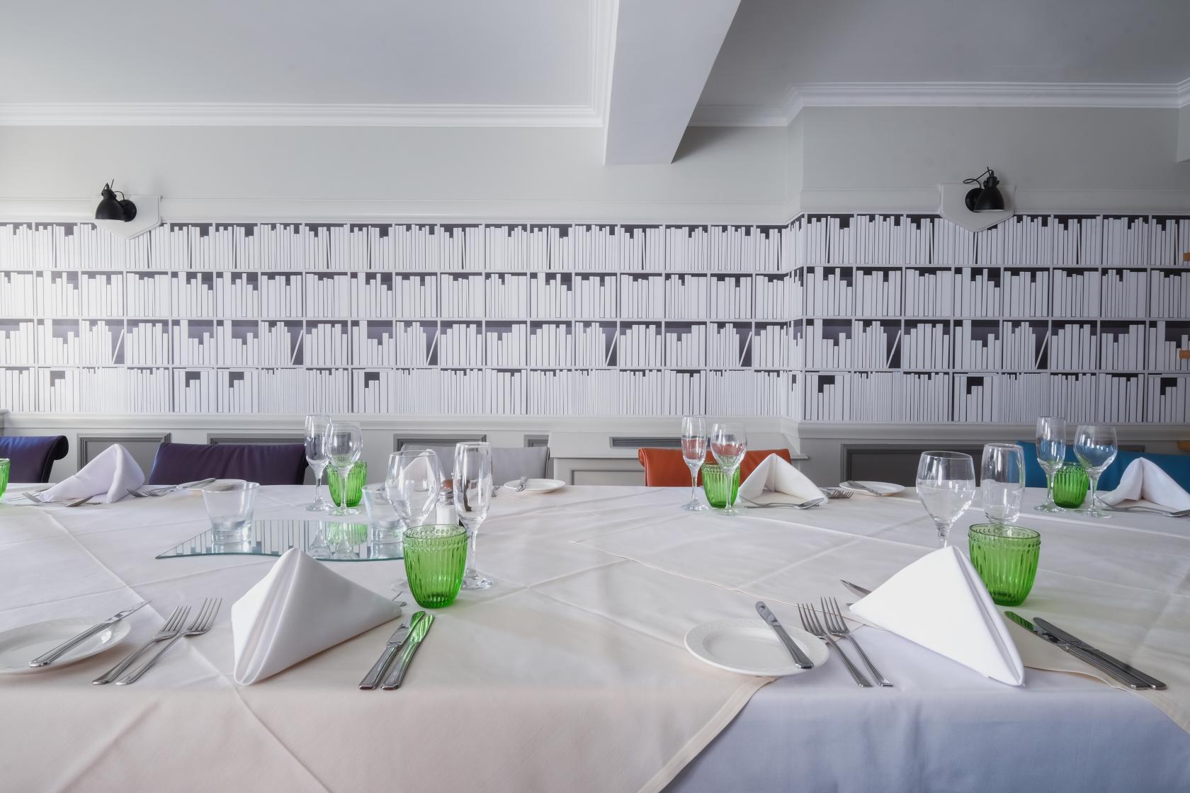 A hotel meeting room with long tables set with glassware, napkins, and patterned wallpaper at Aztec Hotel & Spa.