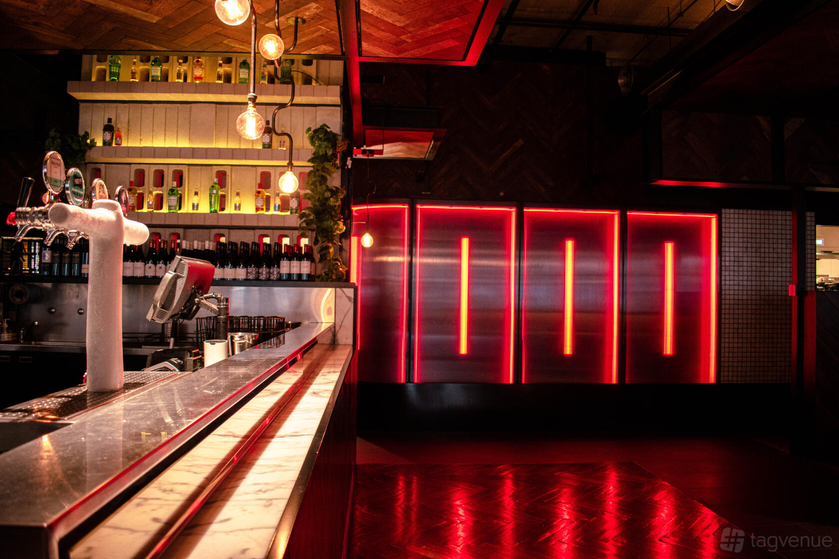 A pub lounge with a marble bar, illuminated shelves of bottles, and red neon accent lighting at Ludlow Bar.