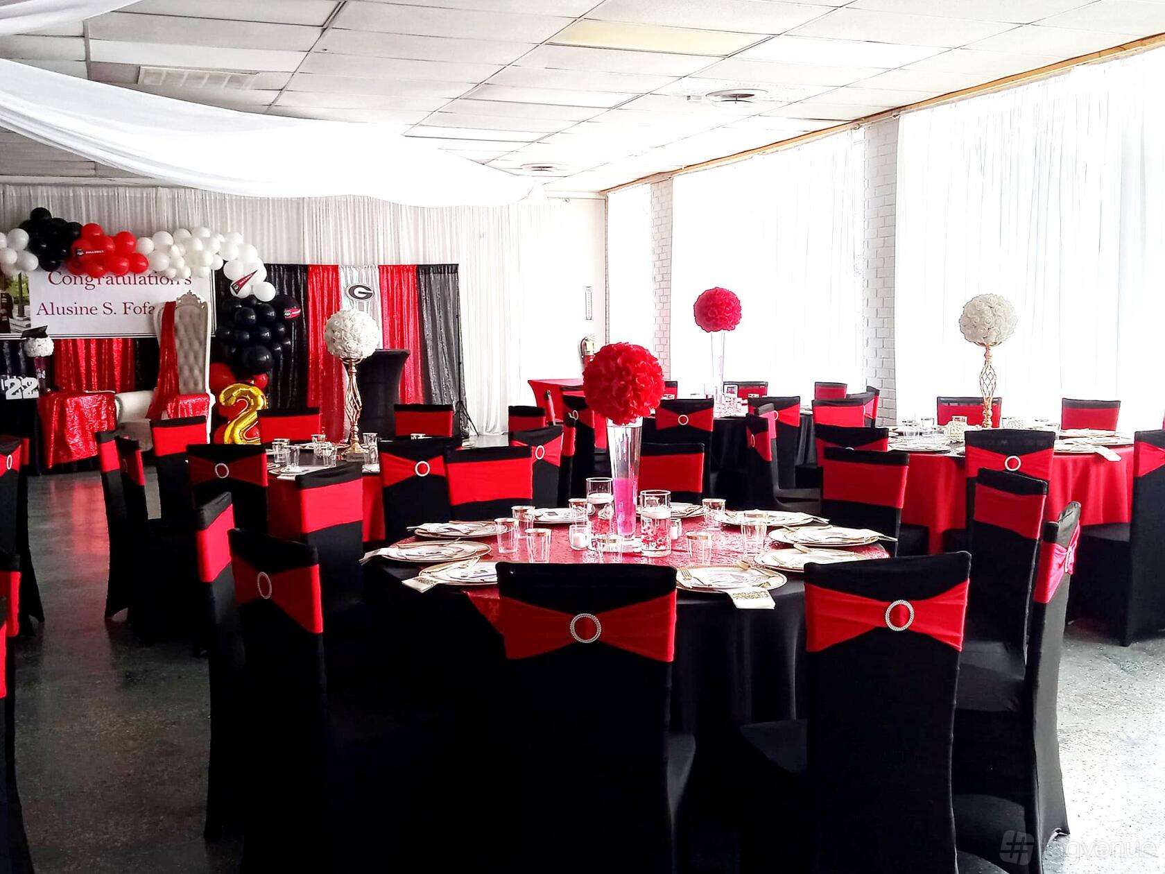 A ballroom with round tables covered in black and red linens, banquet chairs, and balloon decorations at Kaycee's Event Creations Banquet Hall.