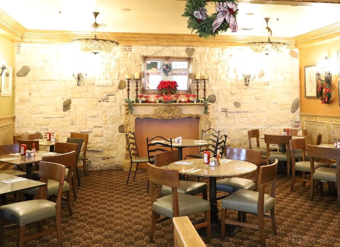 A dining room with round tables, wooden chairs, patterned carpet, and a decorative stone fireplace at Marmalade Cafe - Los Angeles.