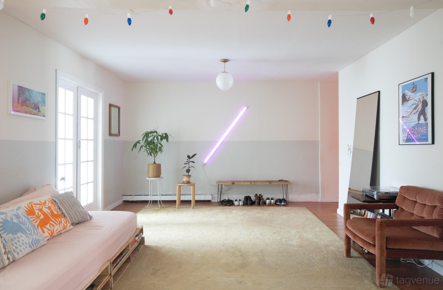 An apartment living room with a pastel sofa, neon wall light, houseplant, and a French door at Playful And Unique Brooklyn Apartment.