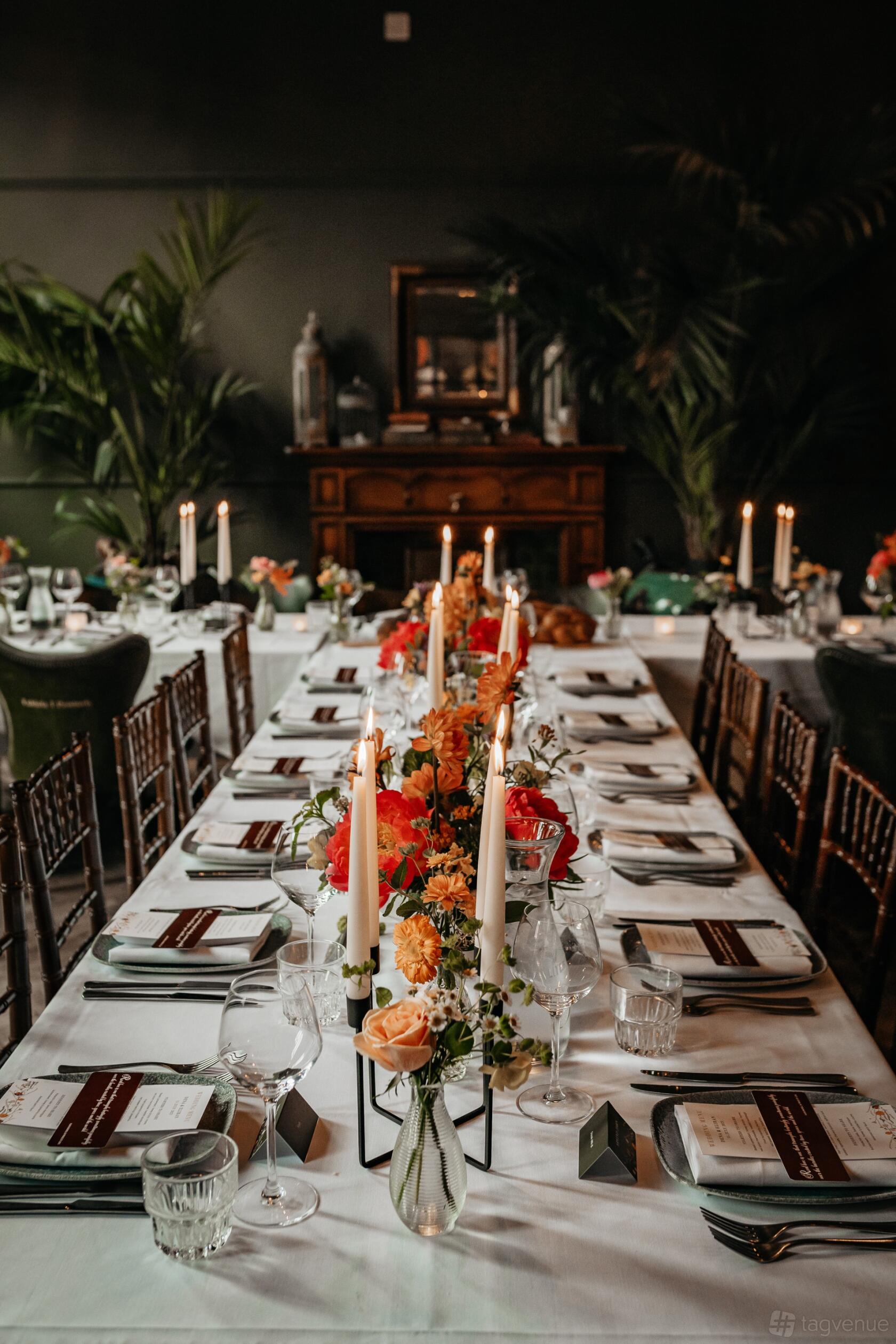 A cocktail bar boardroom with long banquet tables, orange floral centerpieces, and tall candles at The Lost and Found Leeds Club.