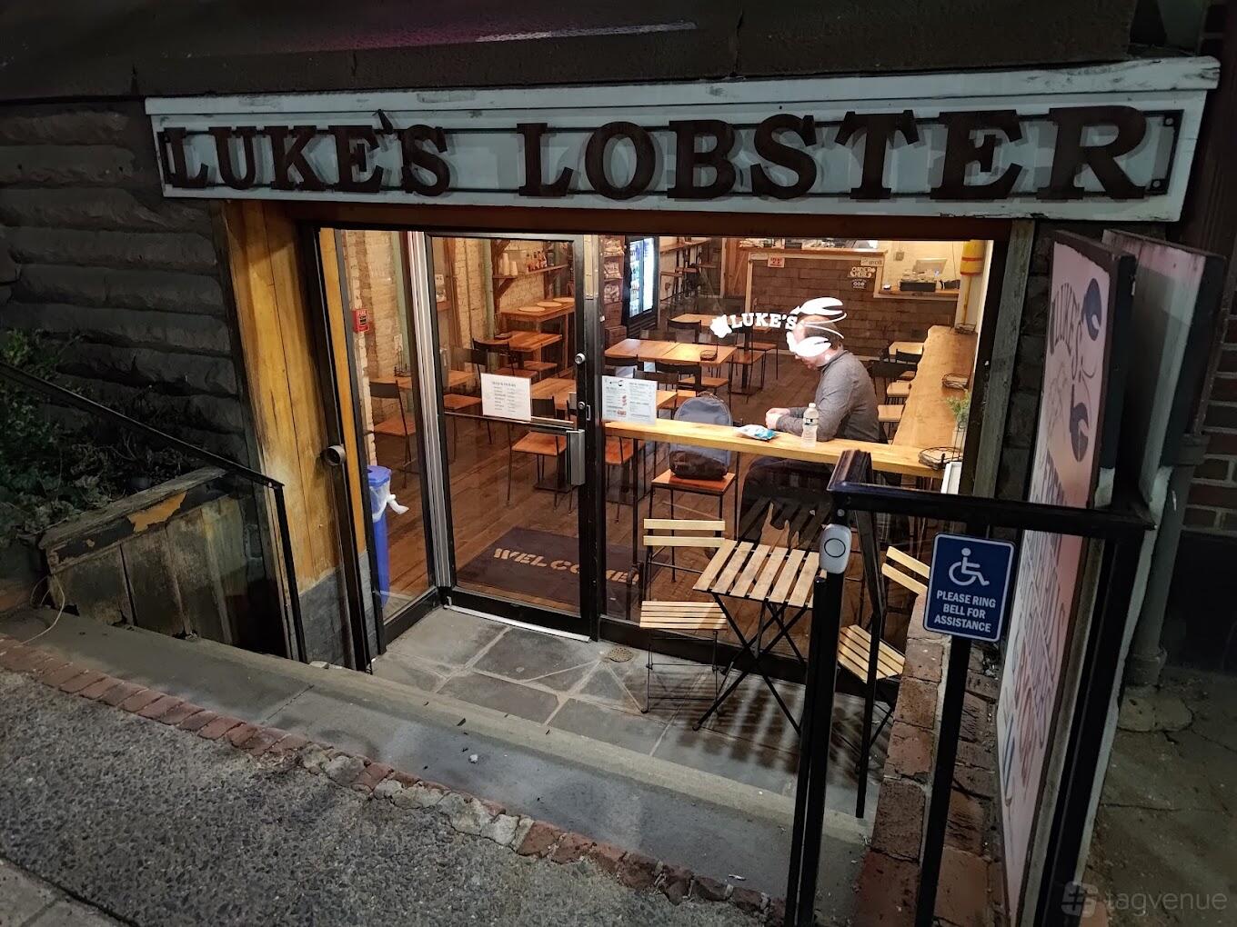 A restaurant with glass entrance doors, wood tables, and visible signage at Luke's Lobster.