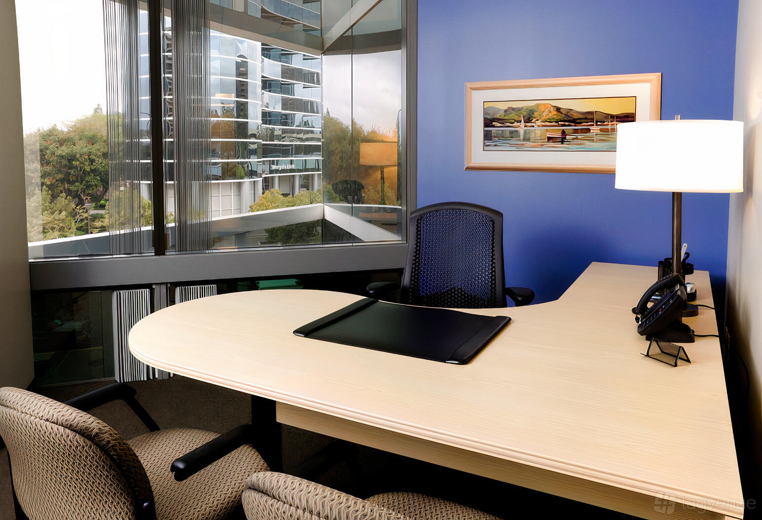 A boardroom with a curved desk, mesh office chair, table lamp, and large corner windows at Intelligent Office - La Jolla.