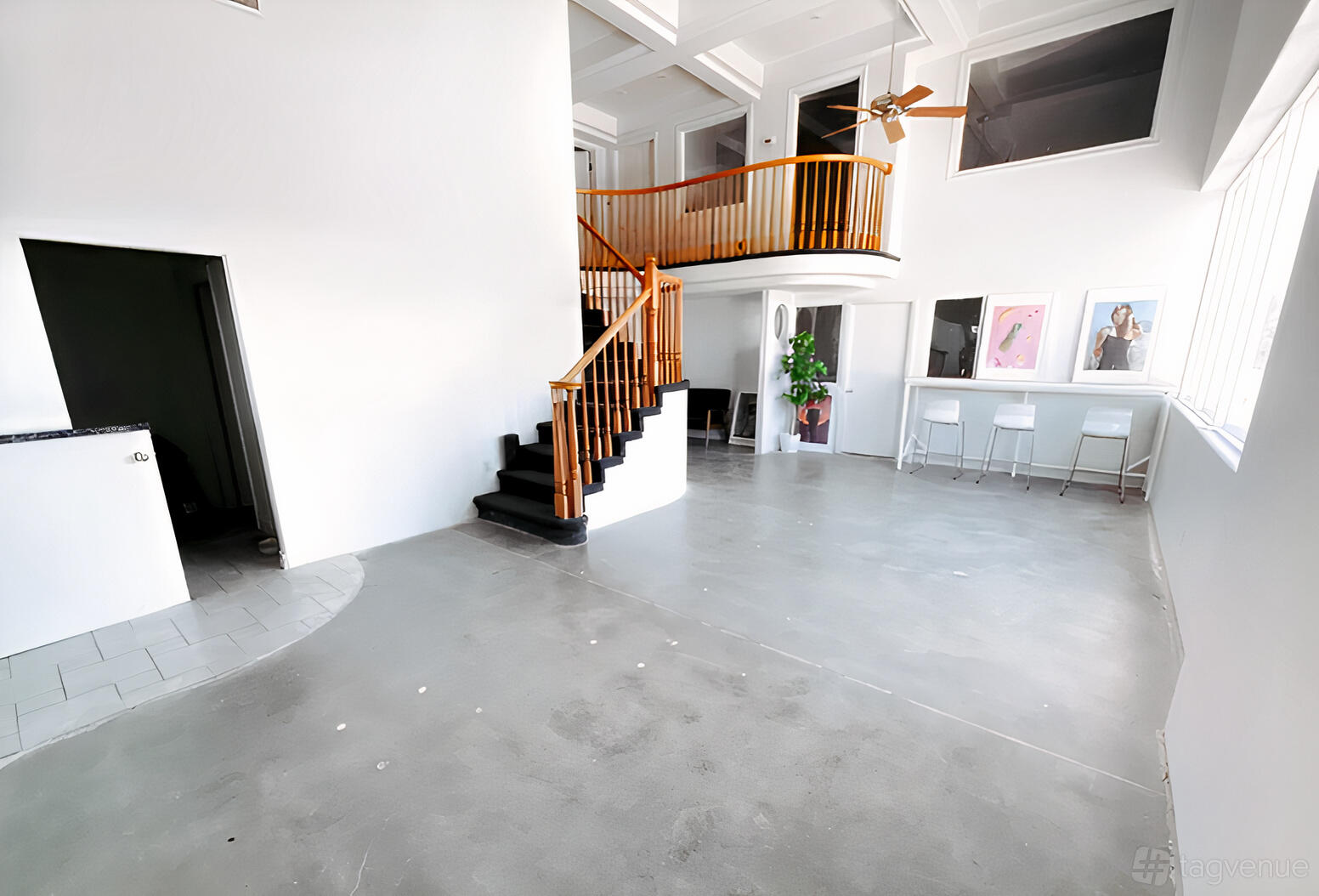 A photo studio with a loft mezzanine, spiral staircase, concrete floor, and large windows at In Color Studios.