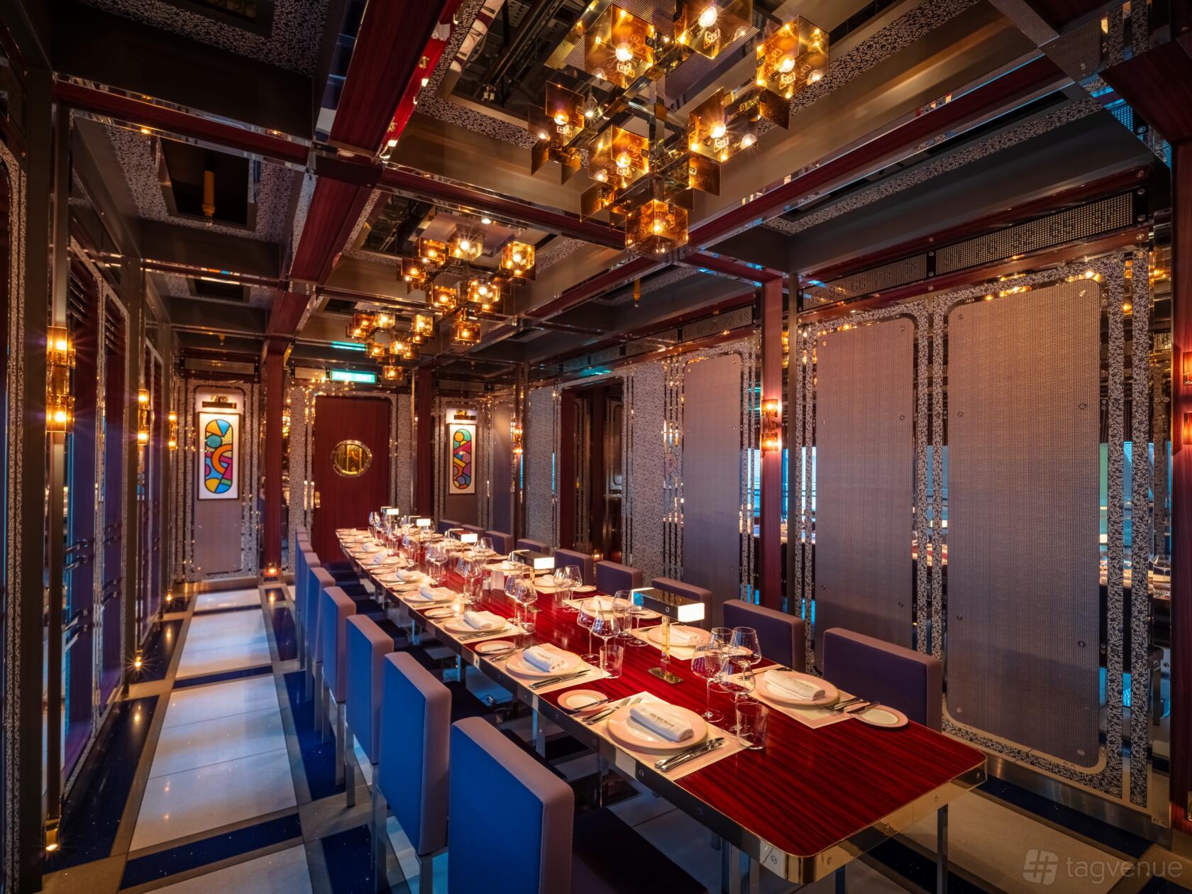 A dining room with a long table set with wine glasses, blue chairs, and stained glass panels at Bob Bob Ricard City.