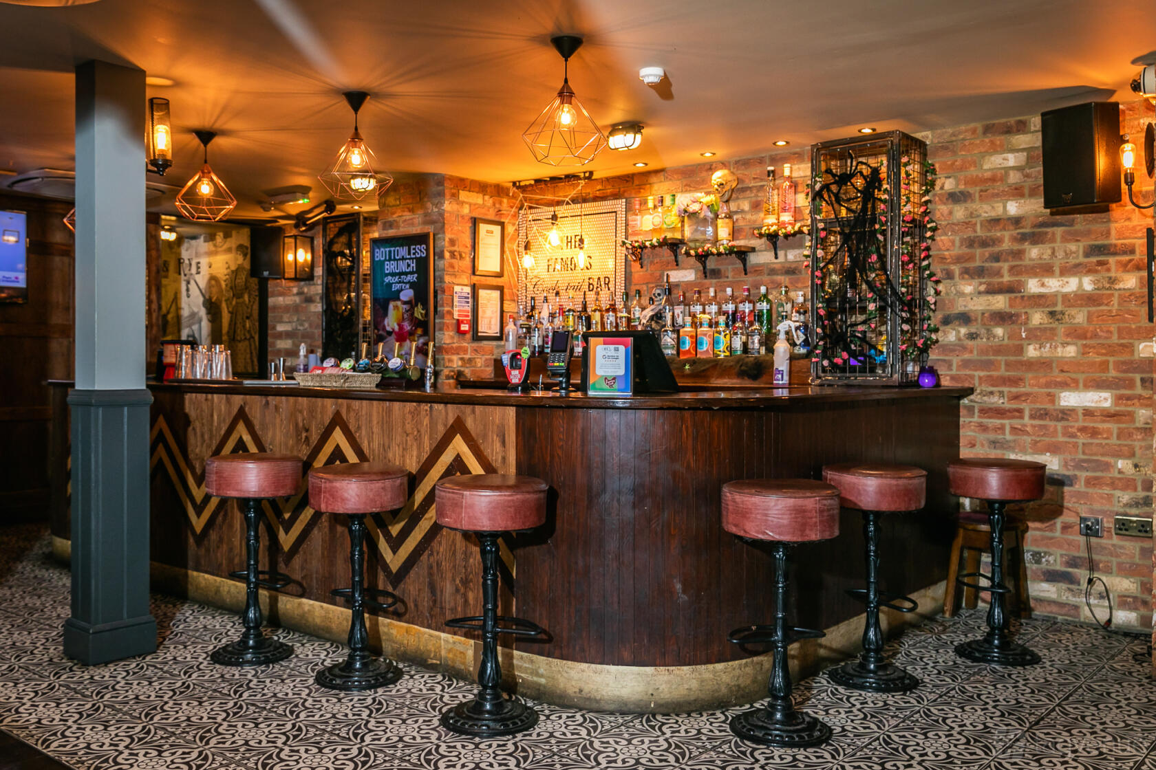 A cocktail bar with exposed brick walls, pendant lighting, and leather bar stools at The Famous Cock Tavern.