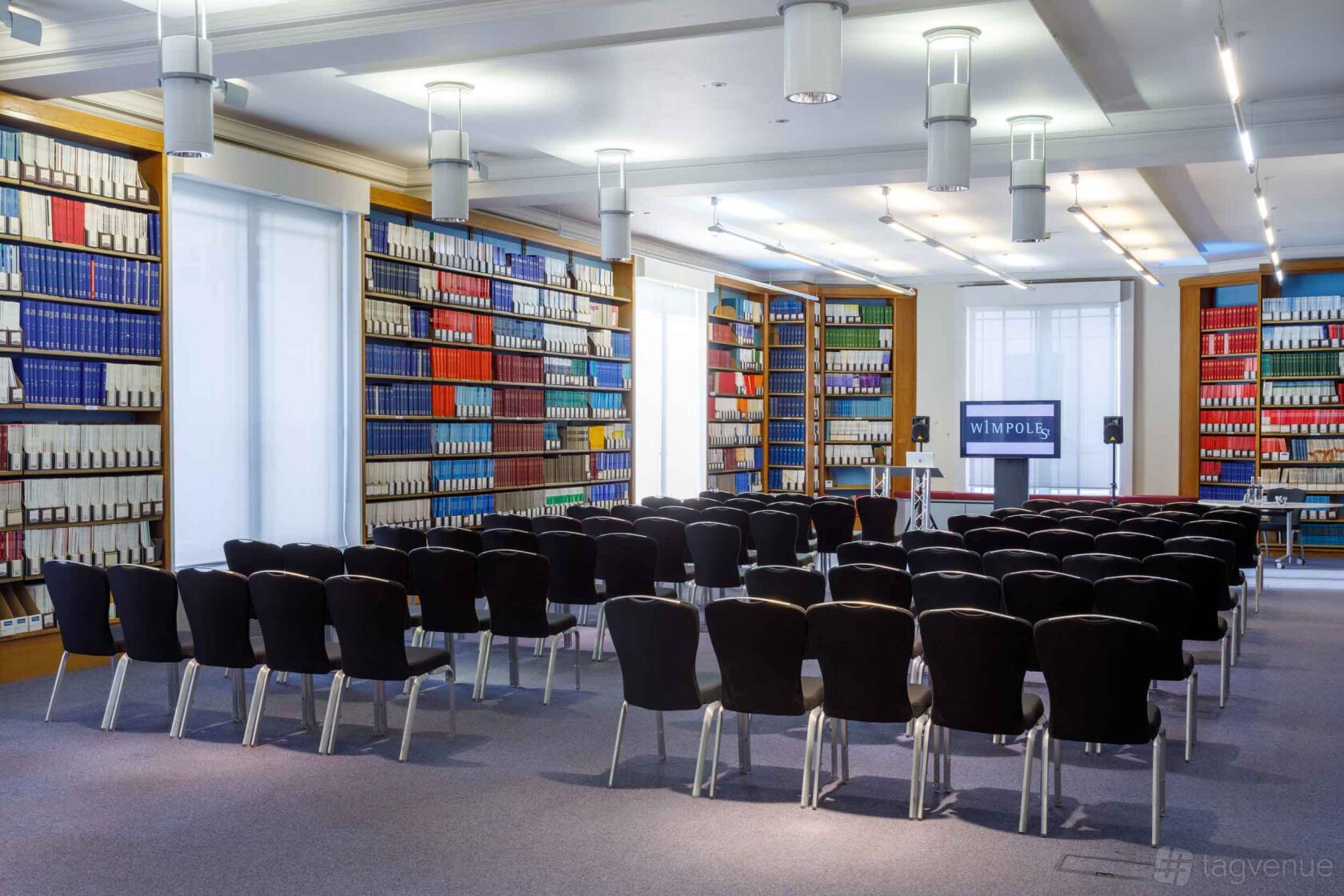 An event room with rows of black chairs, bookshelves lining the walls, and a projector screen at 1 Wimpole Street.
