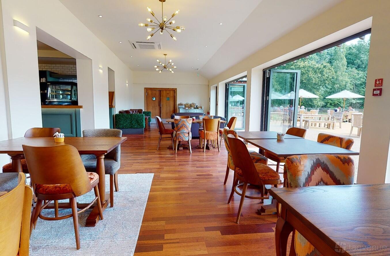 A function room with wooden floors, large windows, and mixed seating at Hampton Court Palace Golf Club.