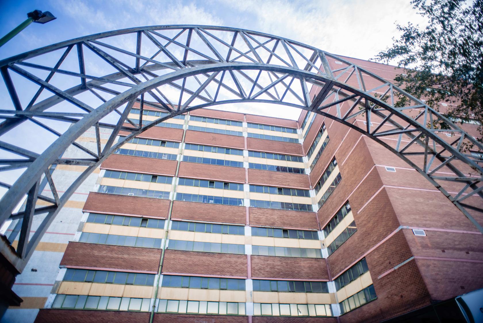 A multi-story brick building with large windows and a metal arch at Archives London.