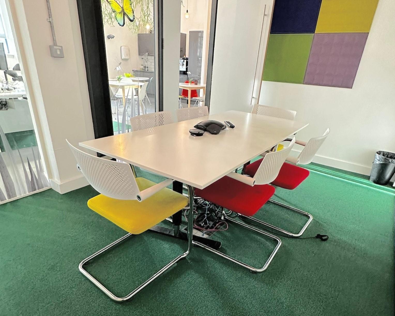 A meeting room with a white table, colorful chairs, phone handset, and green carpet at Synergy Vision.