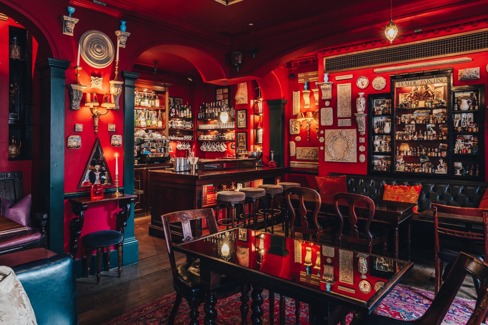 A hotel bar with red walls, vintage decor, mirrored shelves, and velvet seating at The Zetter Marylebone.