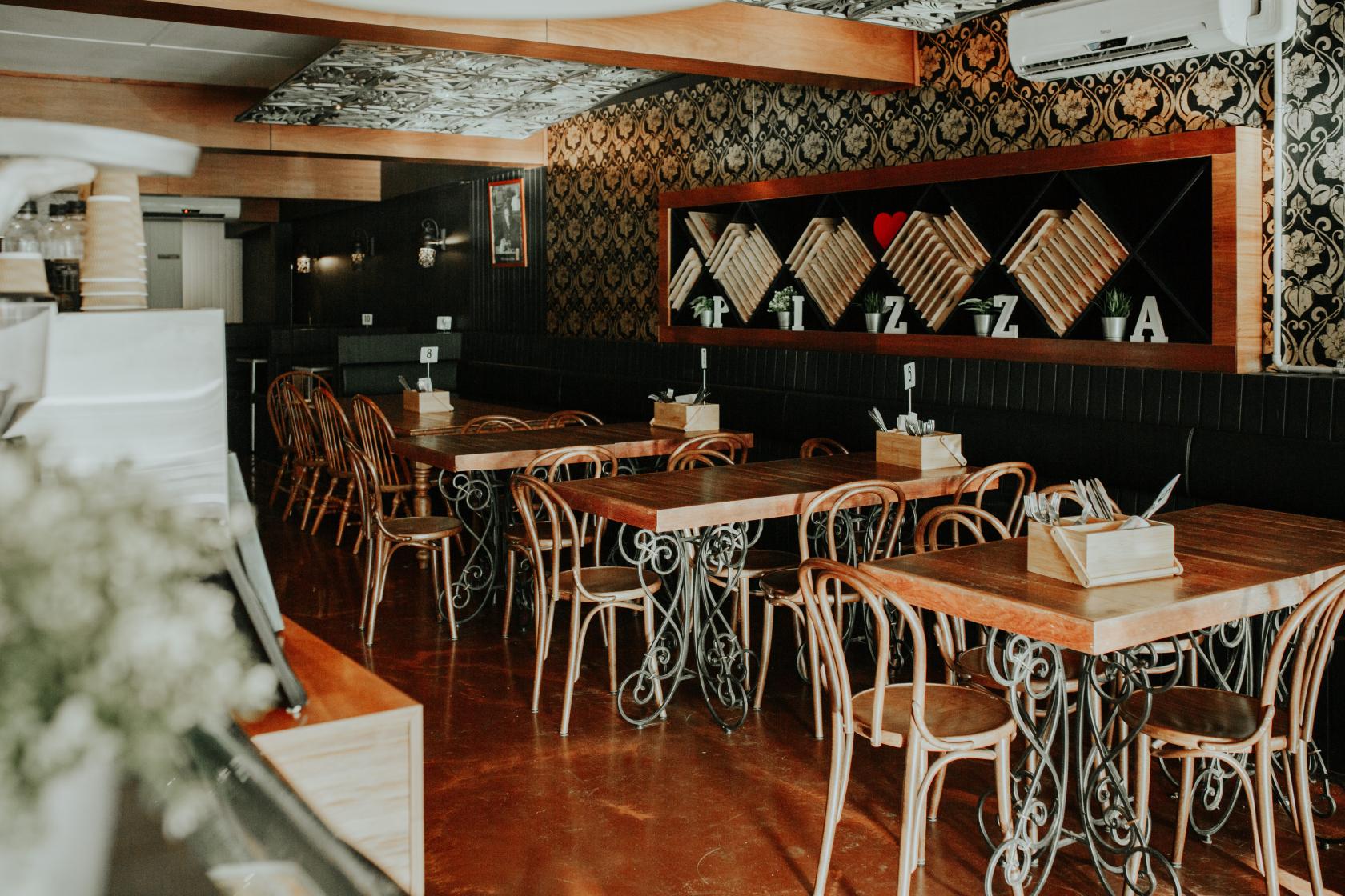 A restaurant with wooden tables, curved chairs, and patterned wallpaper at La Zucca.