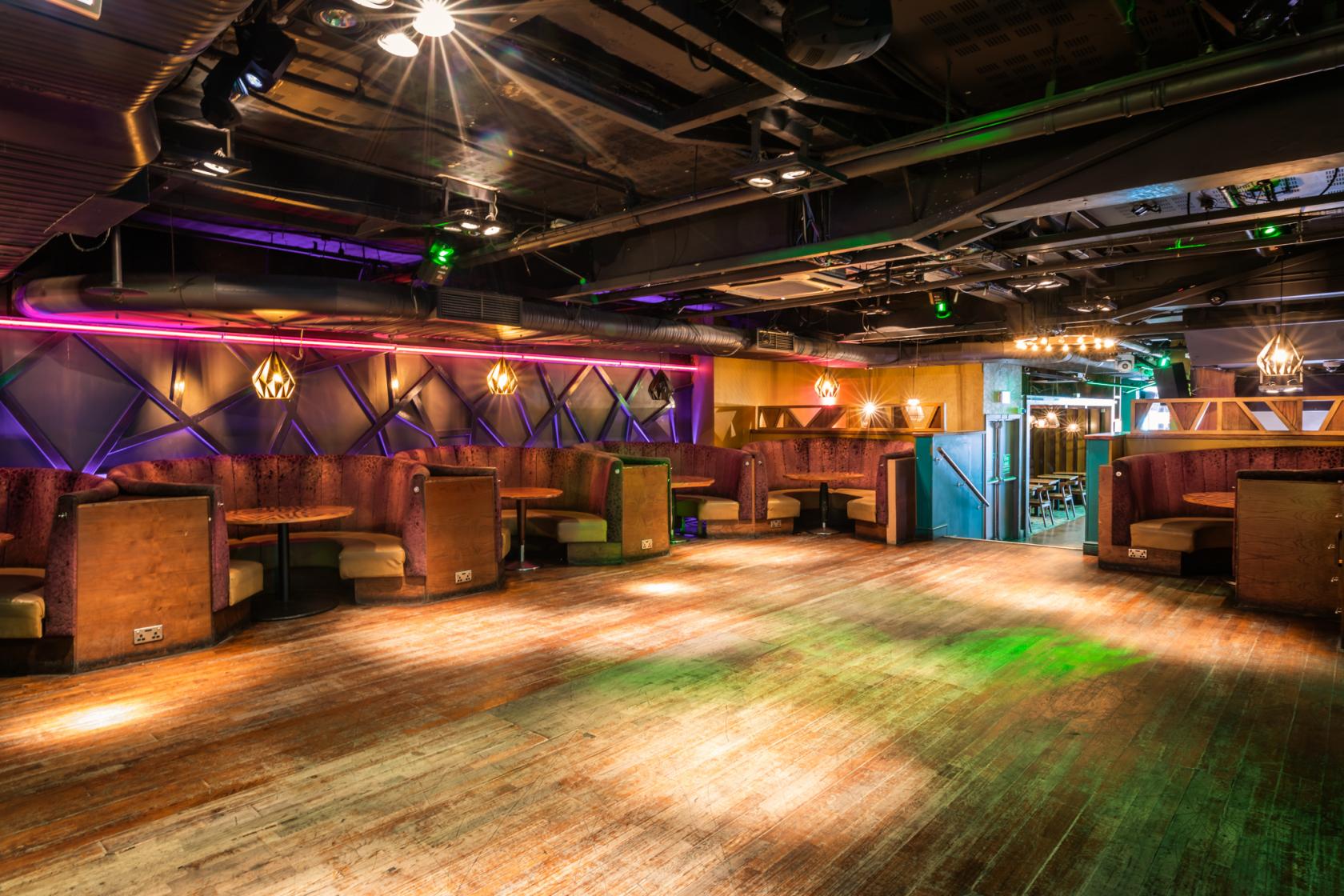 A restaurant in a nightclub with booth seating, neon lighting, and a spacious dance floor at LUXE.