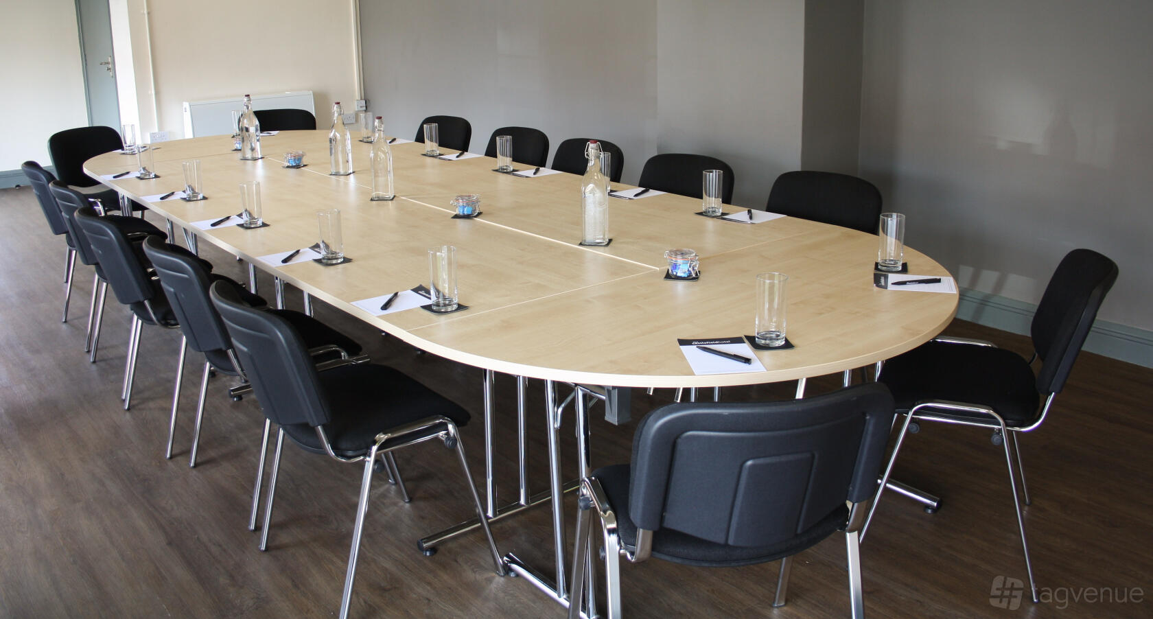 A hotel meeting room with a large oval conference table set with water, glasses, and notepads at Castlefield Hotel.