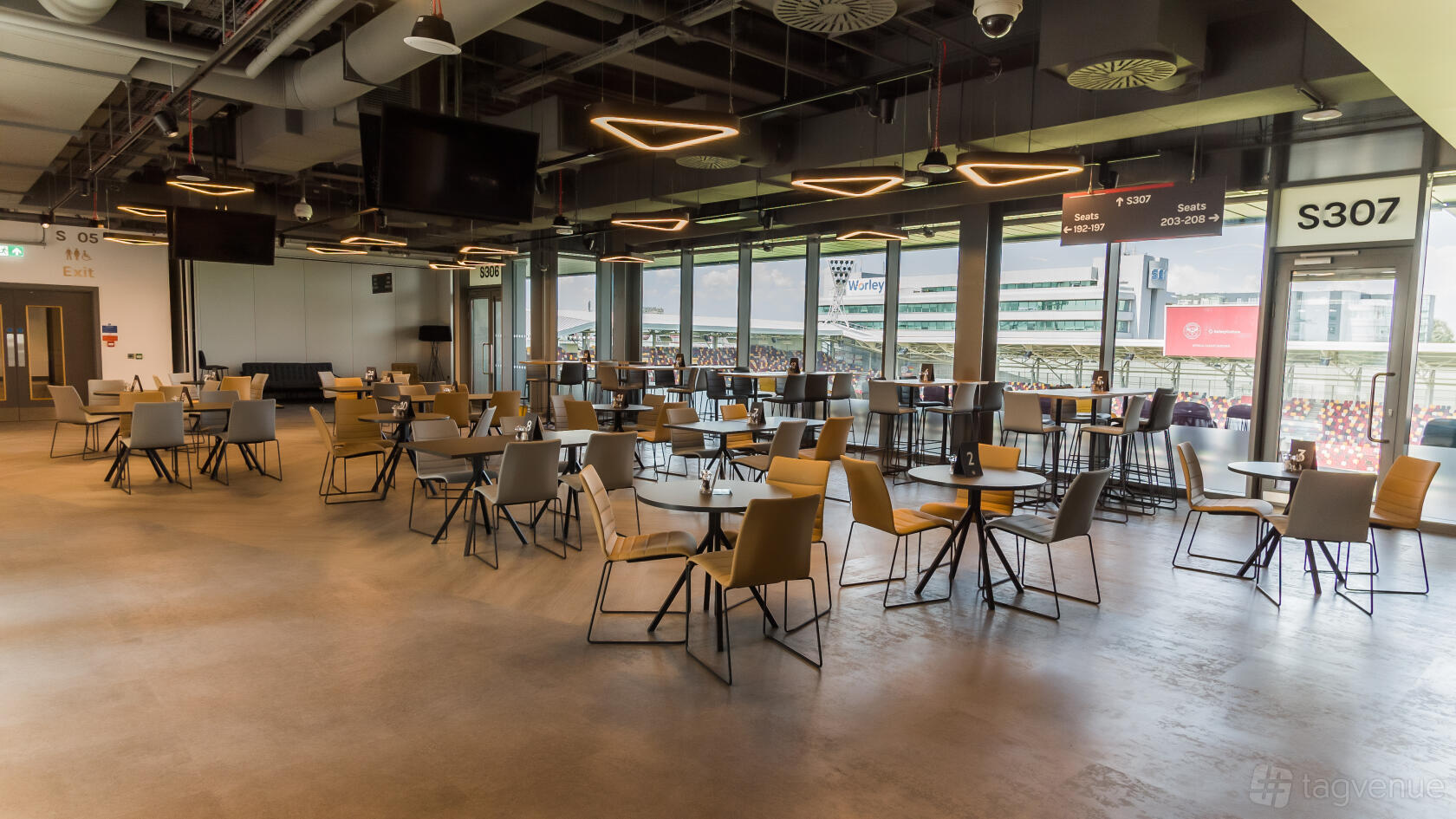 An event venue with floor-to-ceiling windows, round tables, and modern pendant lighting at Brentford Football Club.